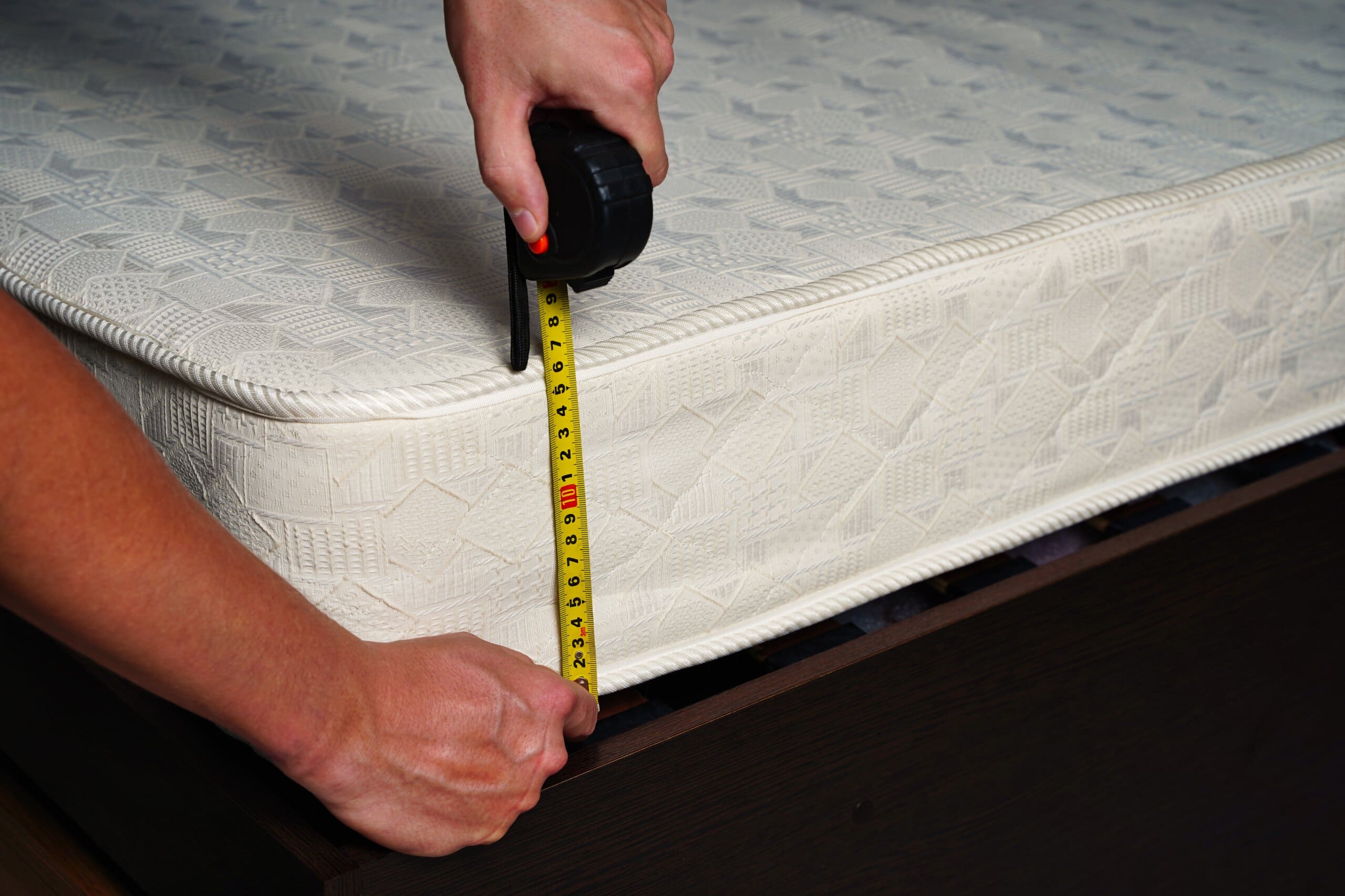 Cropped close up of man's hands measuring mattress depth with a tape measure.