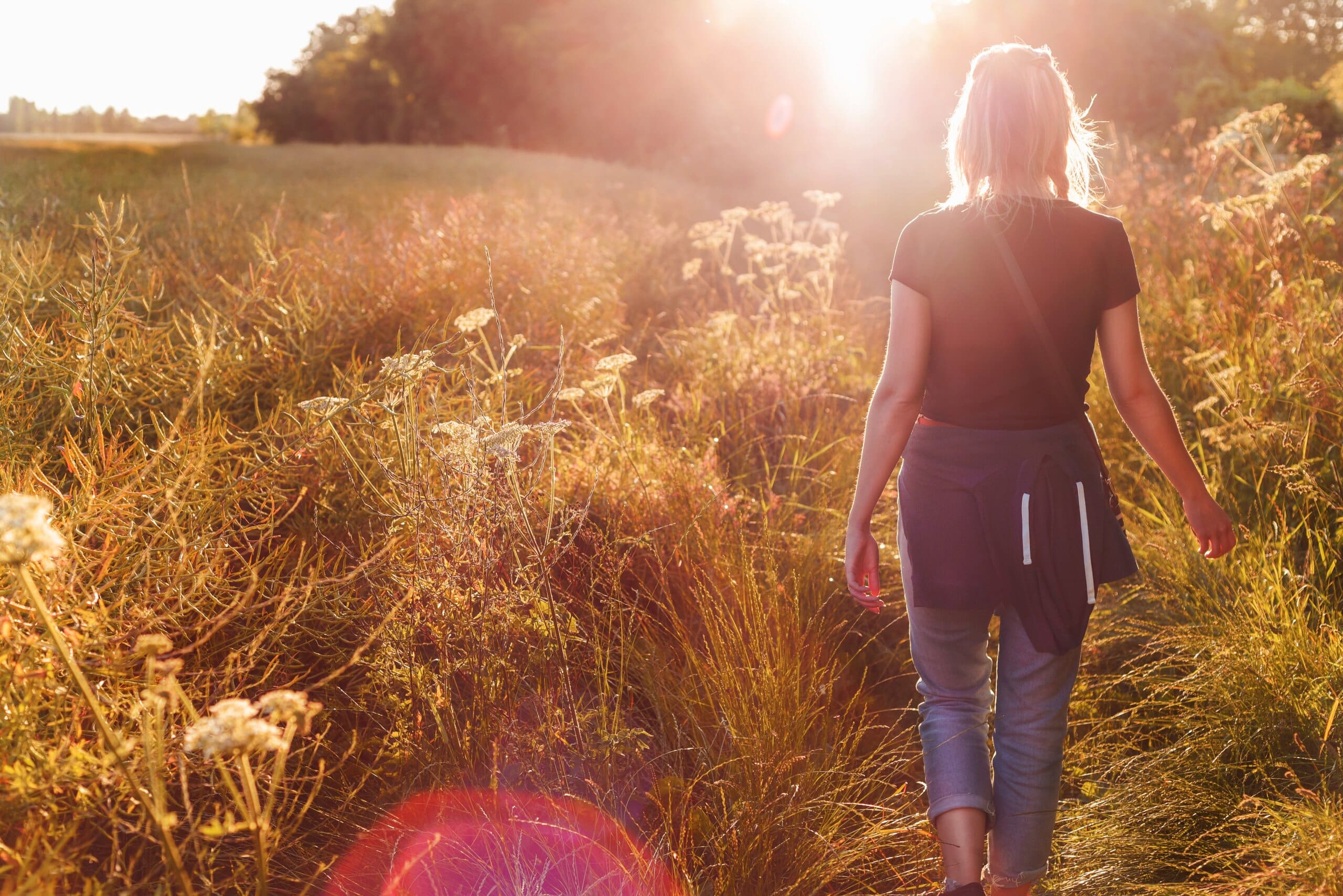 Woman walking through a field with sun shining.