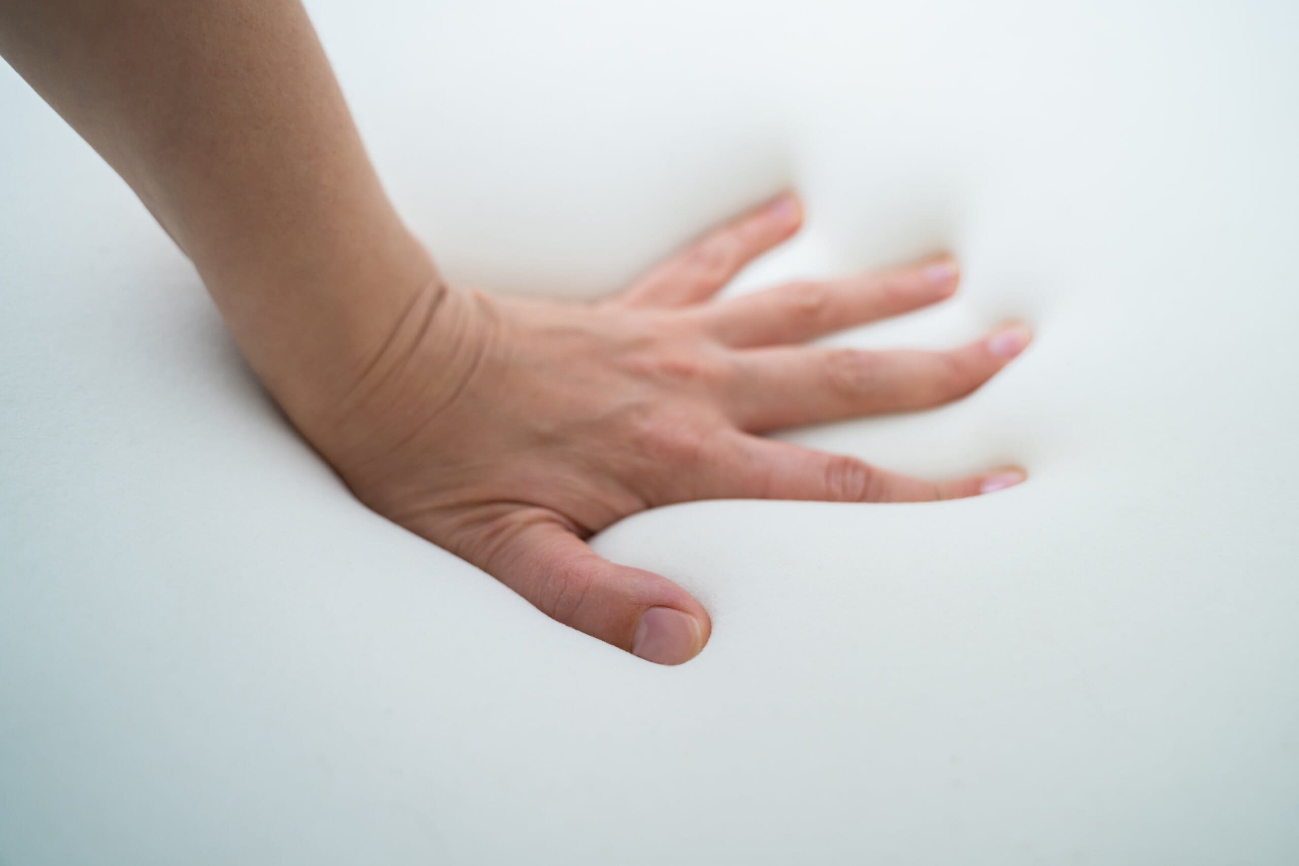 A hand pressing down onto a memory foam mattress, leaving an imprint.