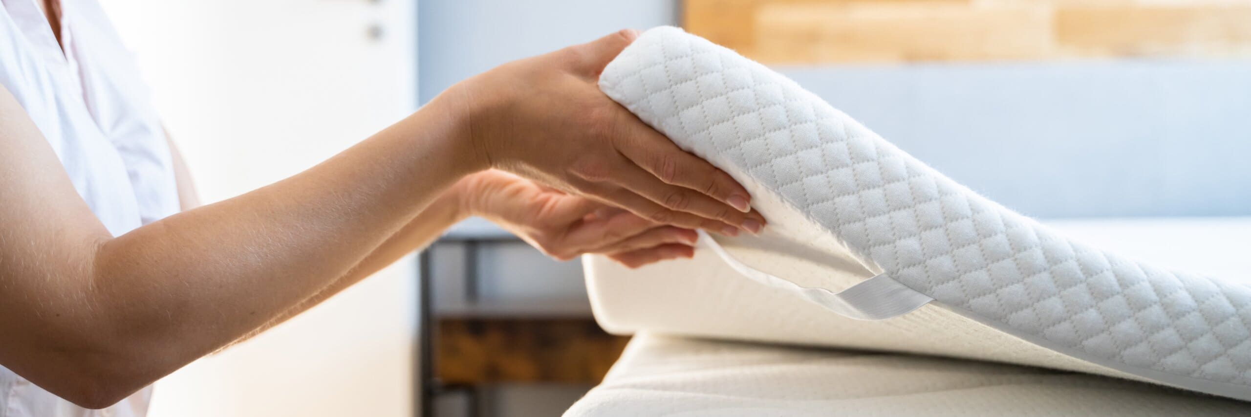 A memory foam mattress topper being placed onto a bed.