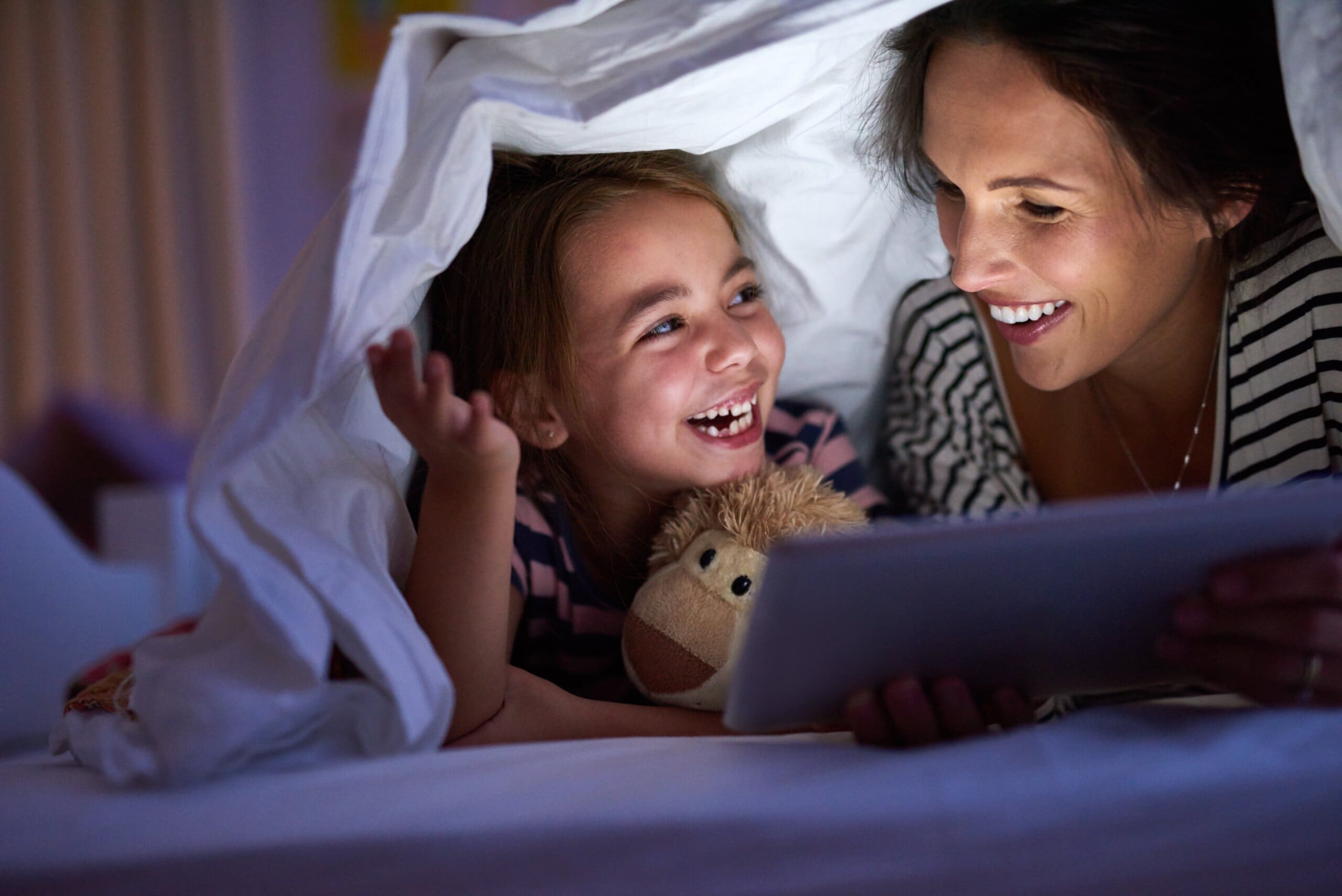 Mother and daughter under the covers reading a bedtime story.