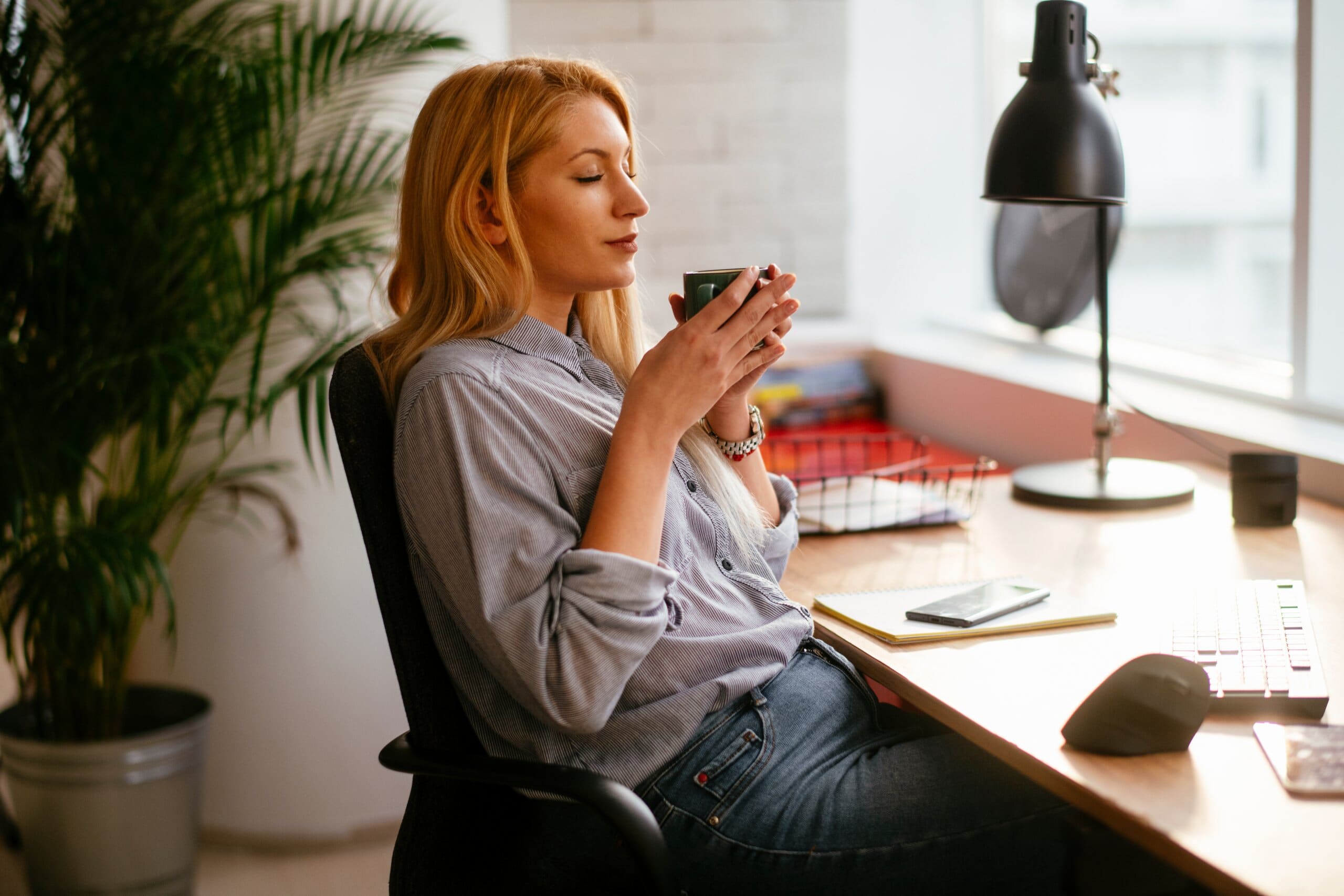 Woman at home desk holding a mug of coffee.