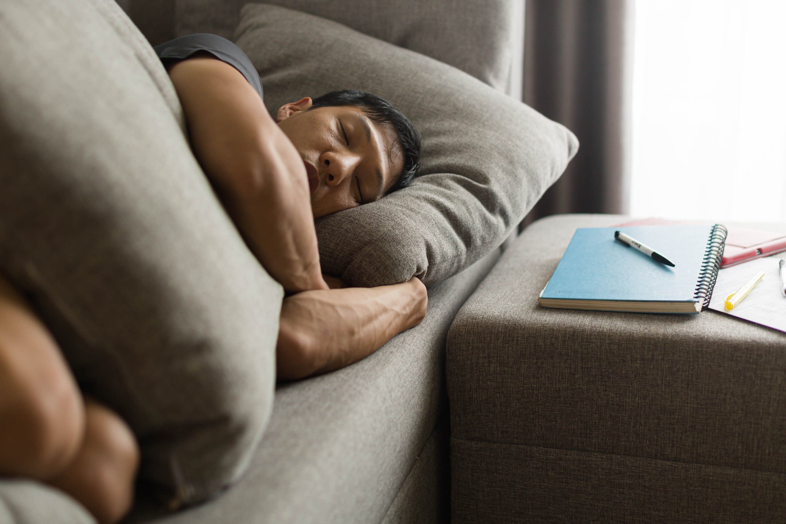 Man sleeping on sofa with notebooks next to him.