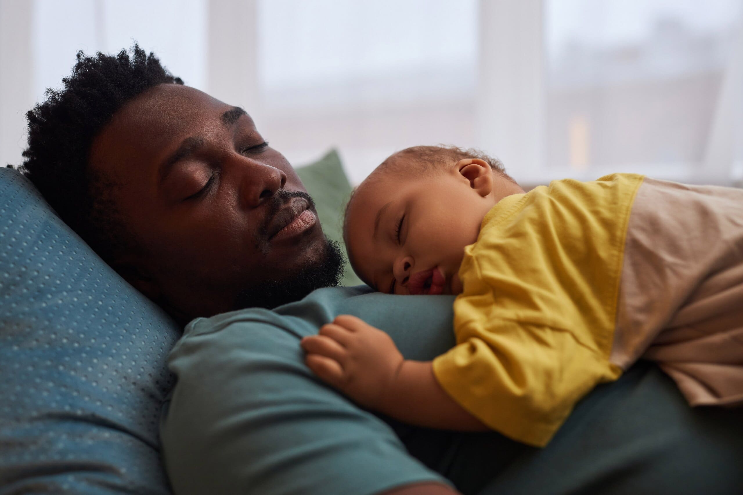Side view of man asleep with a young child sleeping on his chest.