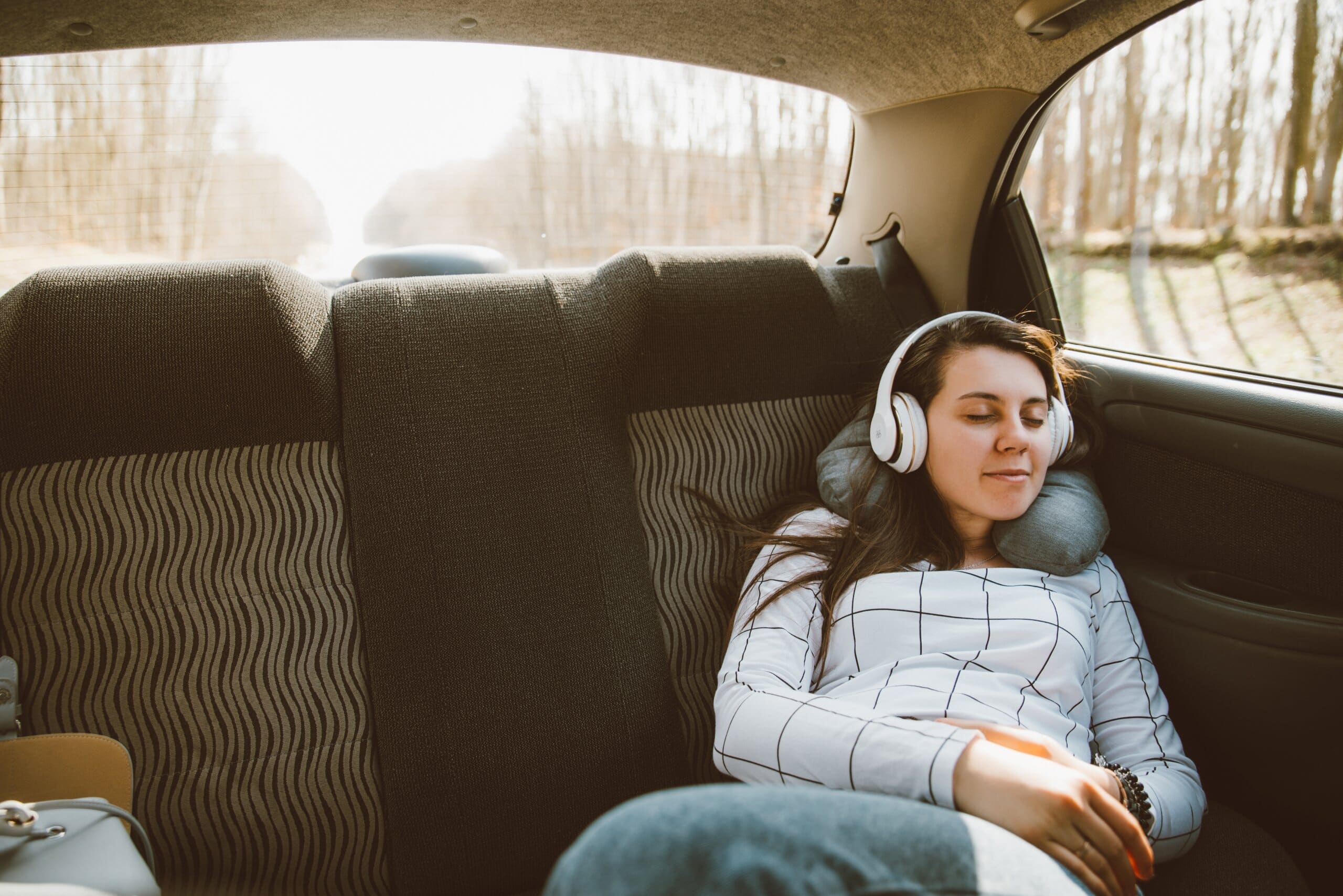 Girl asleep on back seat of car with neck pillow and headphones.