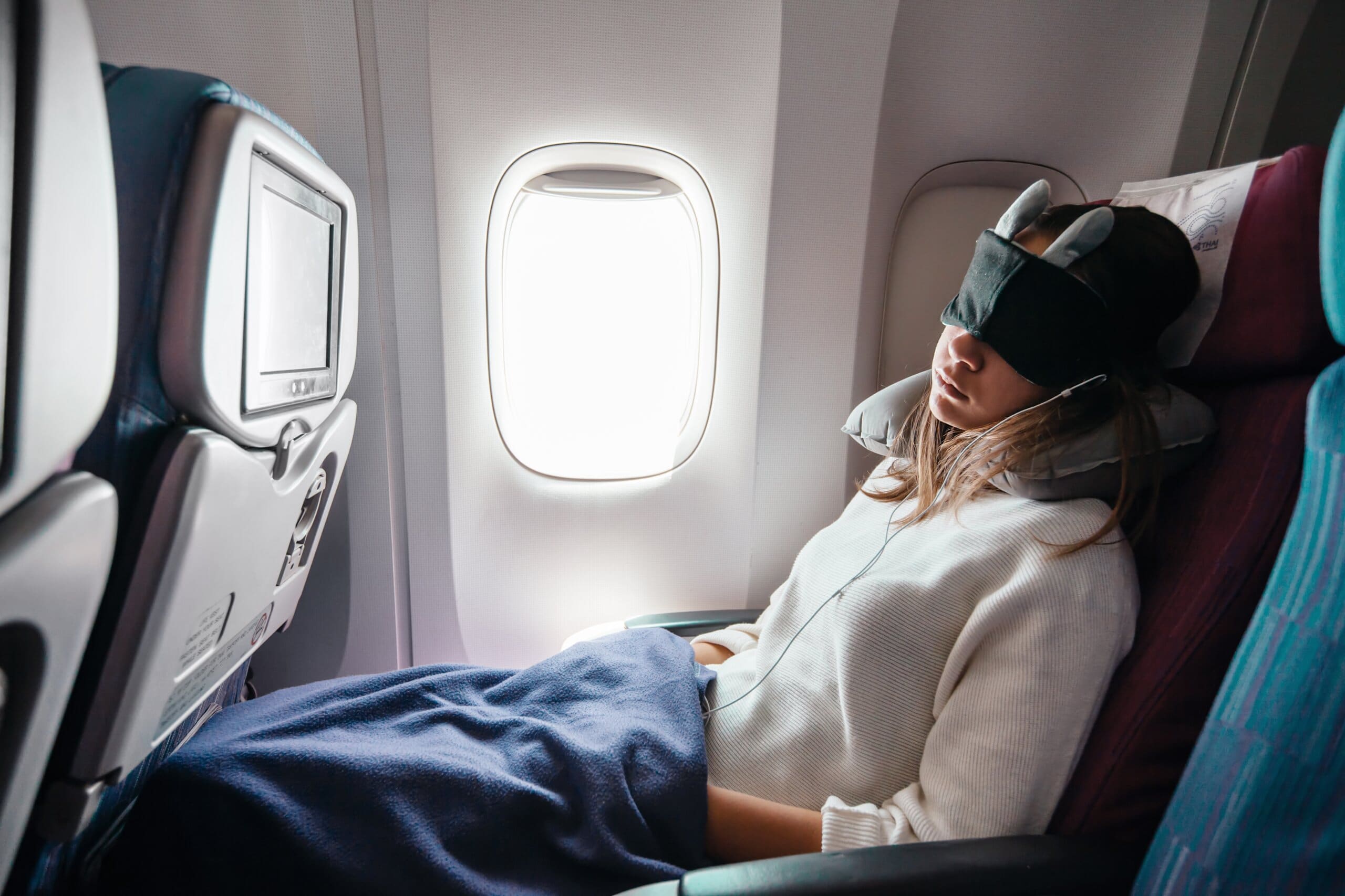 Girl sleeping on a plane with a neck pillow, blanket and eye mask.