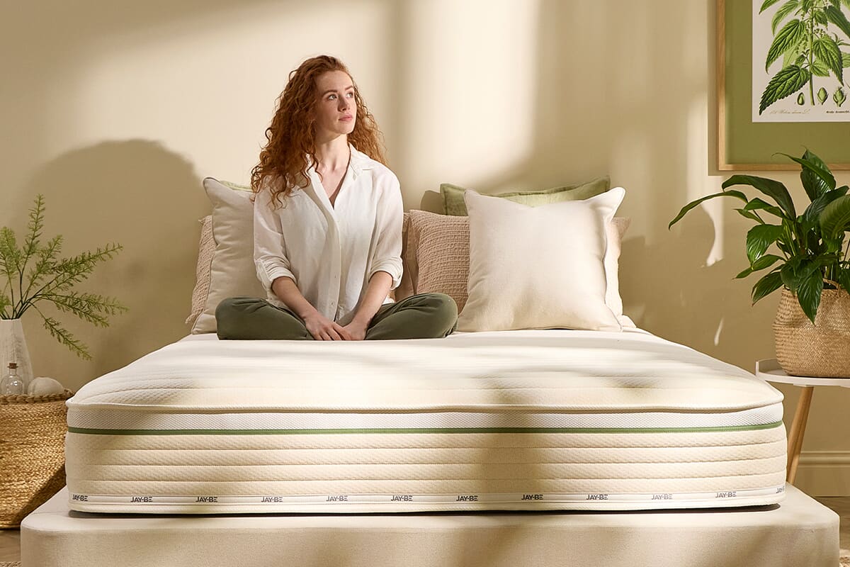 The Jay-Be Nettle hybrid mattress with a red-haired lady sitting atop, cross legged.