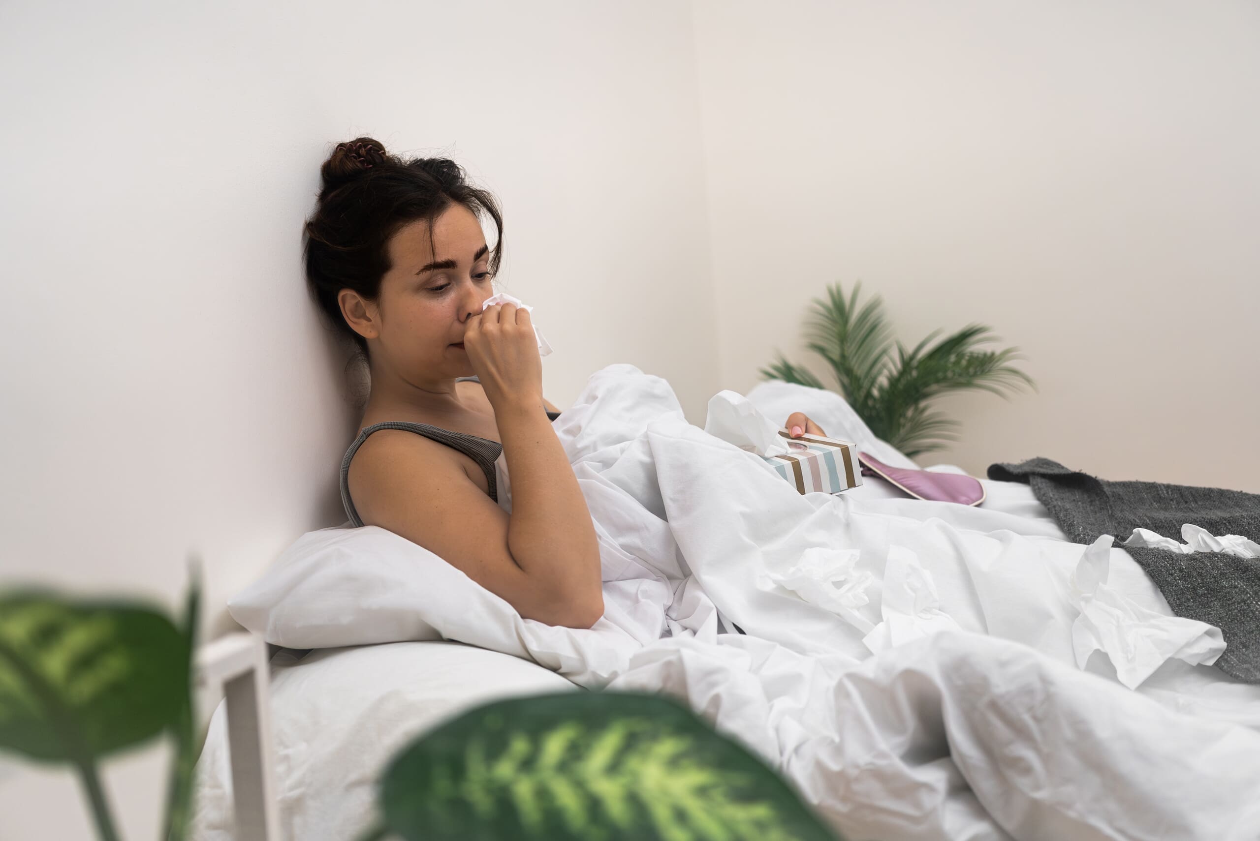 Woman holding tissue to her nose laying in bed.