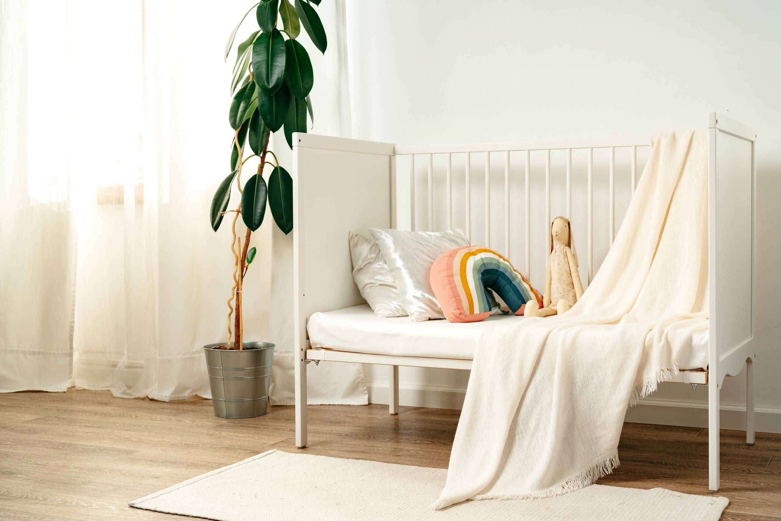 White wooden cot bed with modern decor and a house plant to the left.