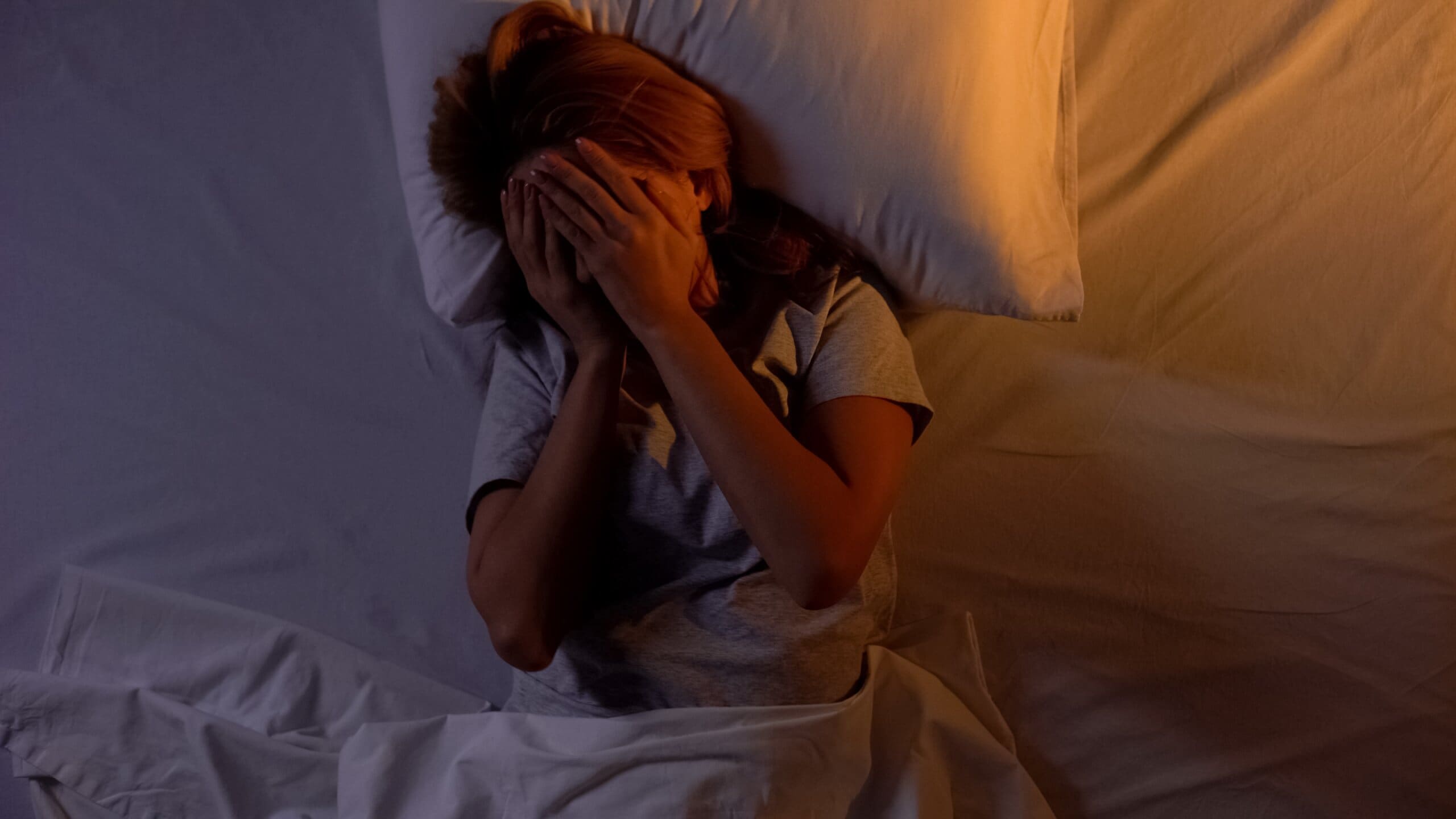 Woman hiding face while lying in bed, after experiencing a night terror.