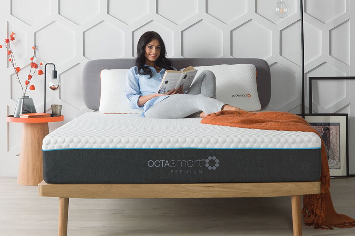Woman laying on the Octasmart Premium Deluxe Mattress reading a book and smiling at the camera.