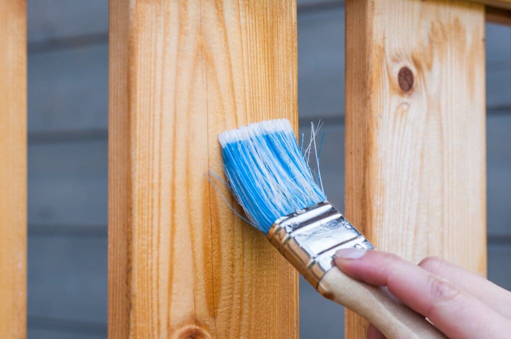 Paintbrush with blue paint painting wooden fence