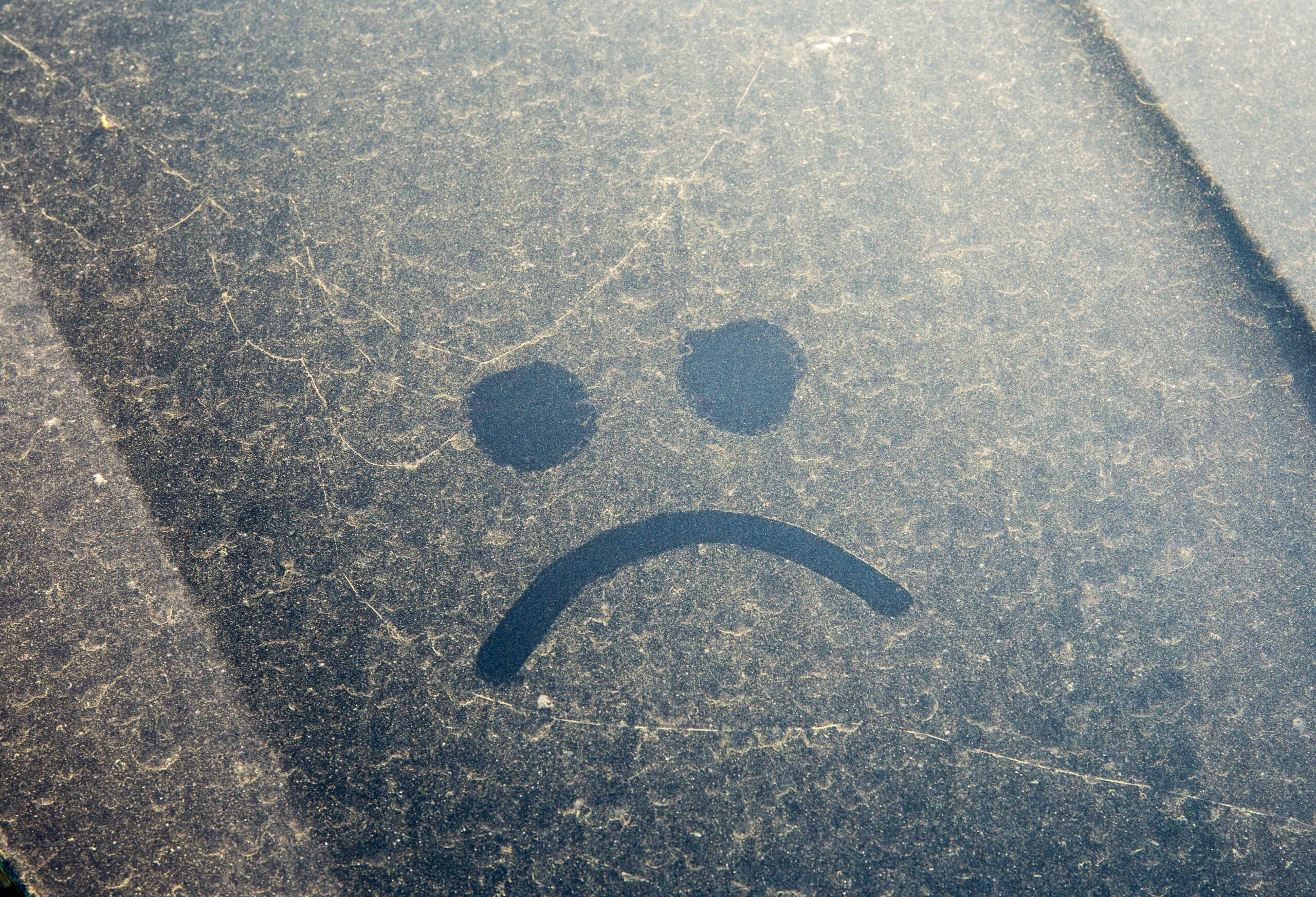 Sad face drawn in pollen covering a car's exterior.