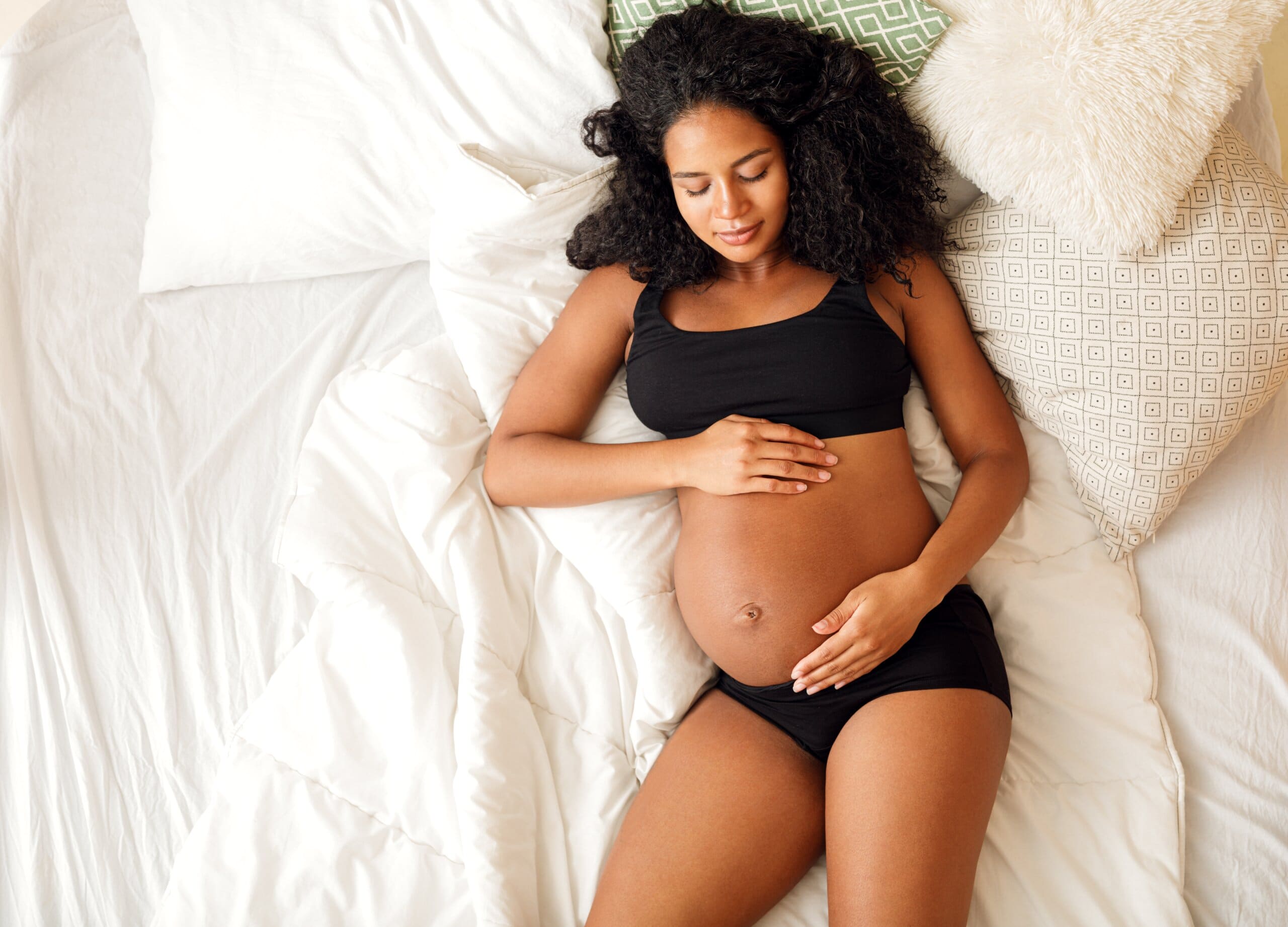 Young black woman holding her pregnant belly in bed.