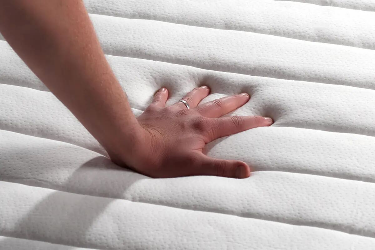 Hand pressing down on a Reflex foam mattress.