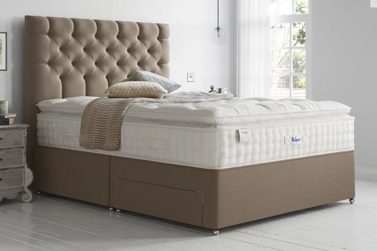 Image of the Relyon Lincoln pillow top mattress on a light brown divan bed with tufted headboard.