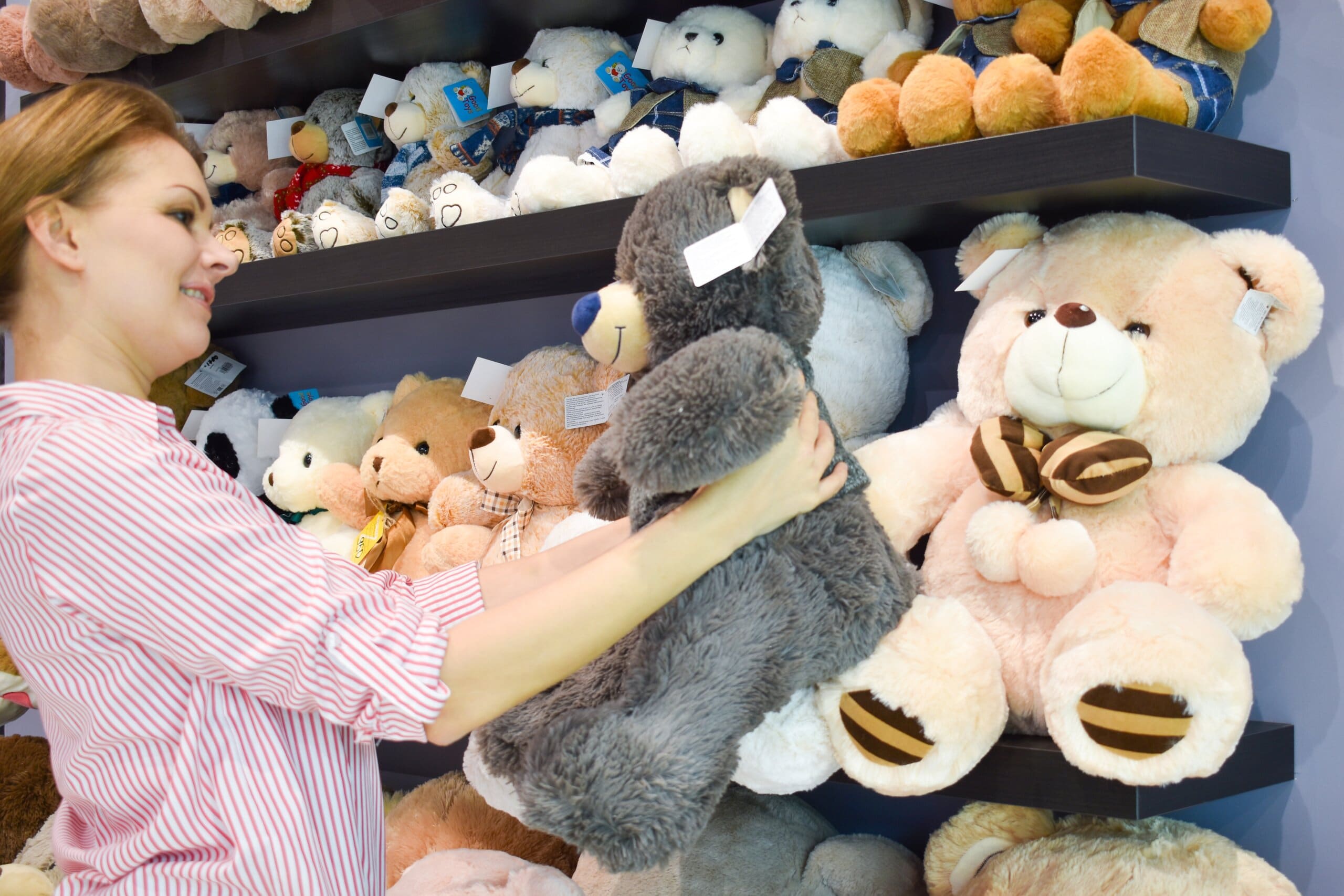 Woman in a toy store selecting a teddy bear.