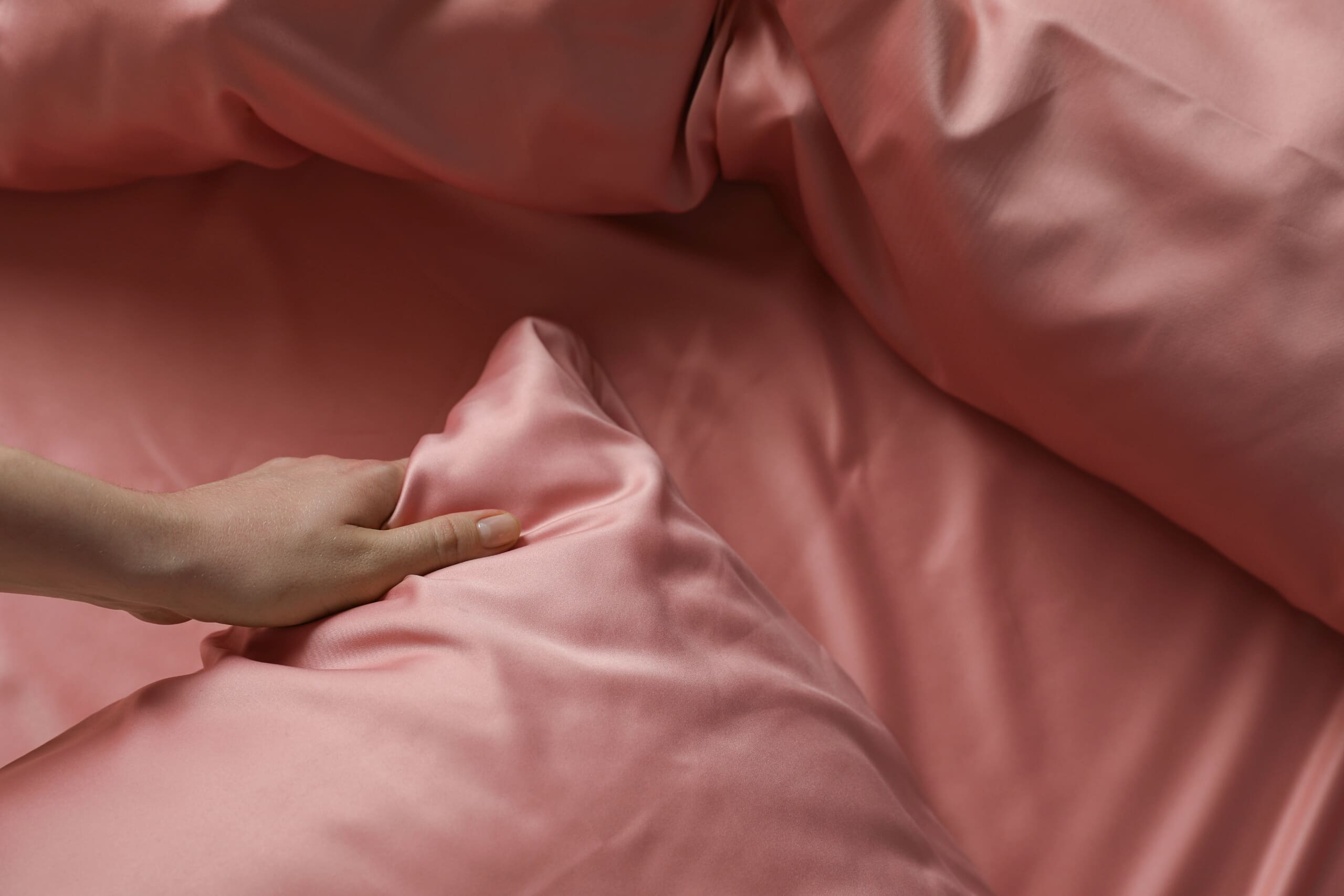 CLose up of woman's hand over pink silk bedding.