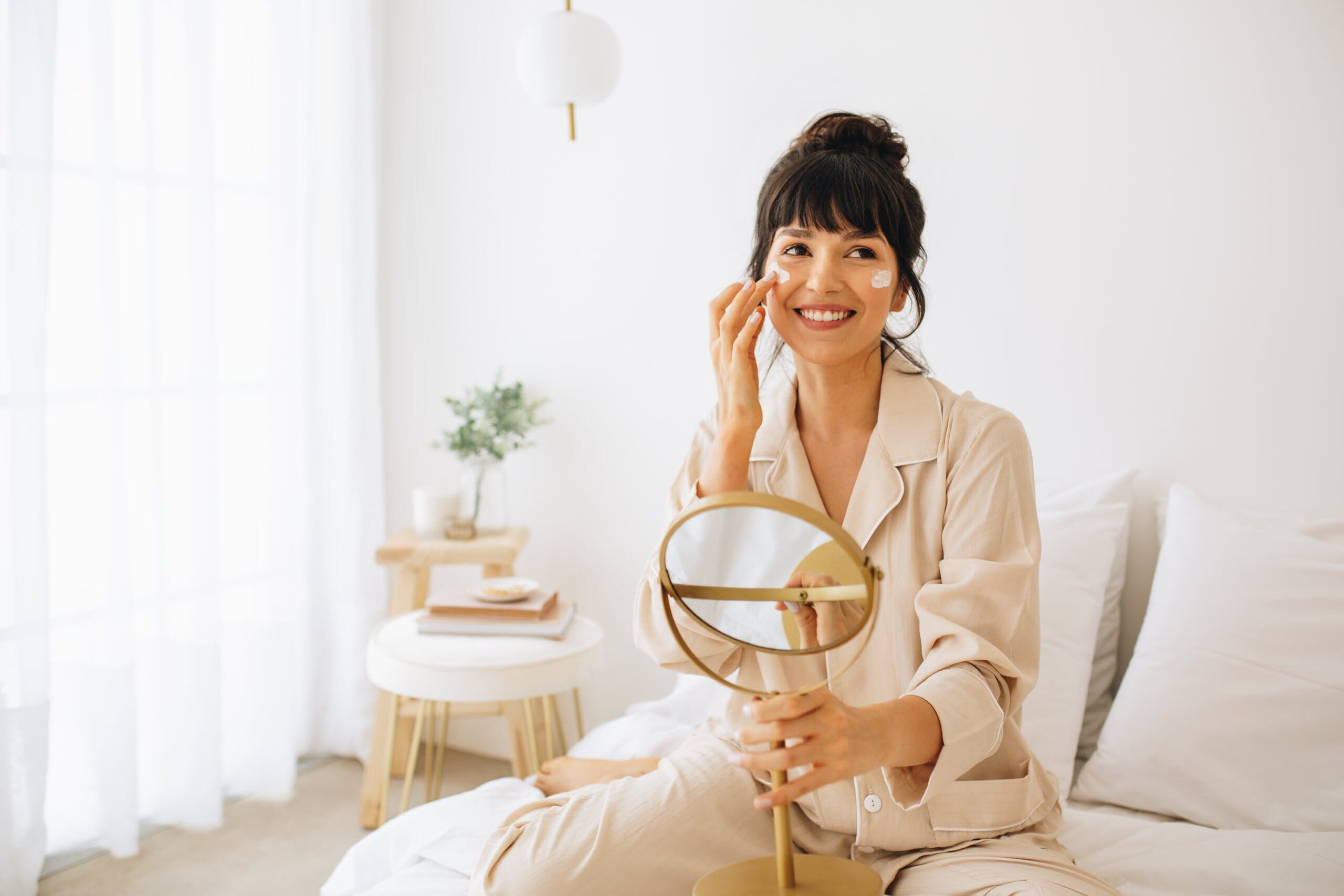 Woman sat on her bed doing her skin care routine.