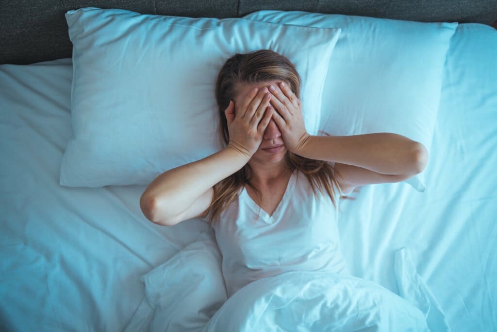 High angle shot of woman lying in bed with hands over face, depicting stress.