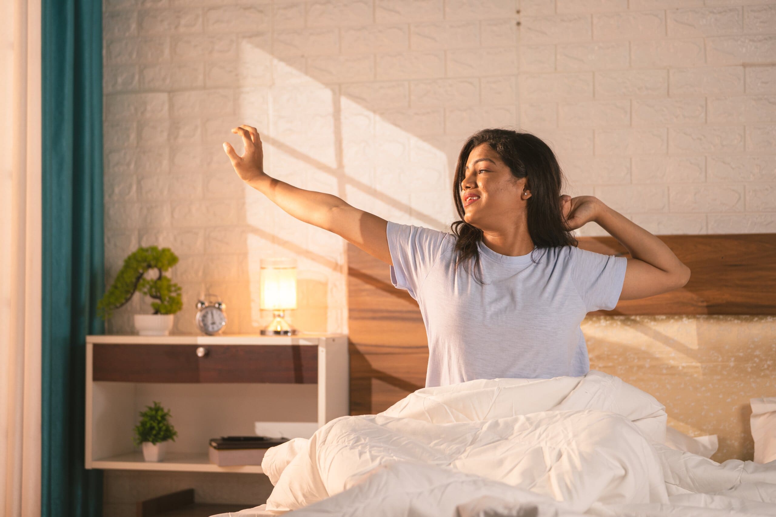 Woman stretching looking happy in bed as sunlight comes through.
