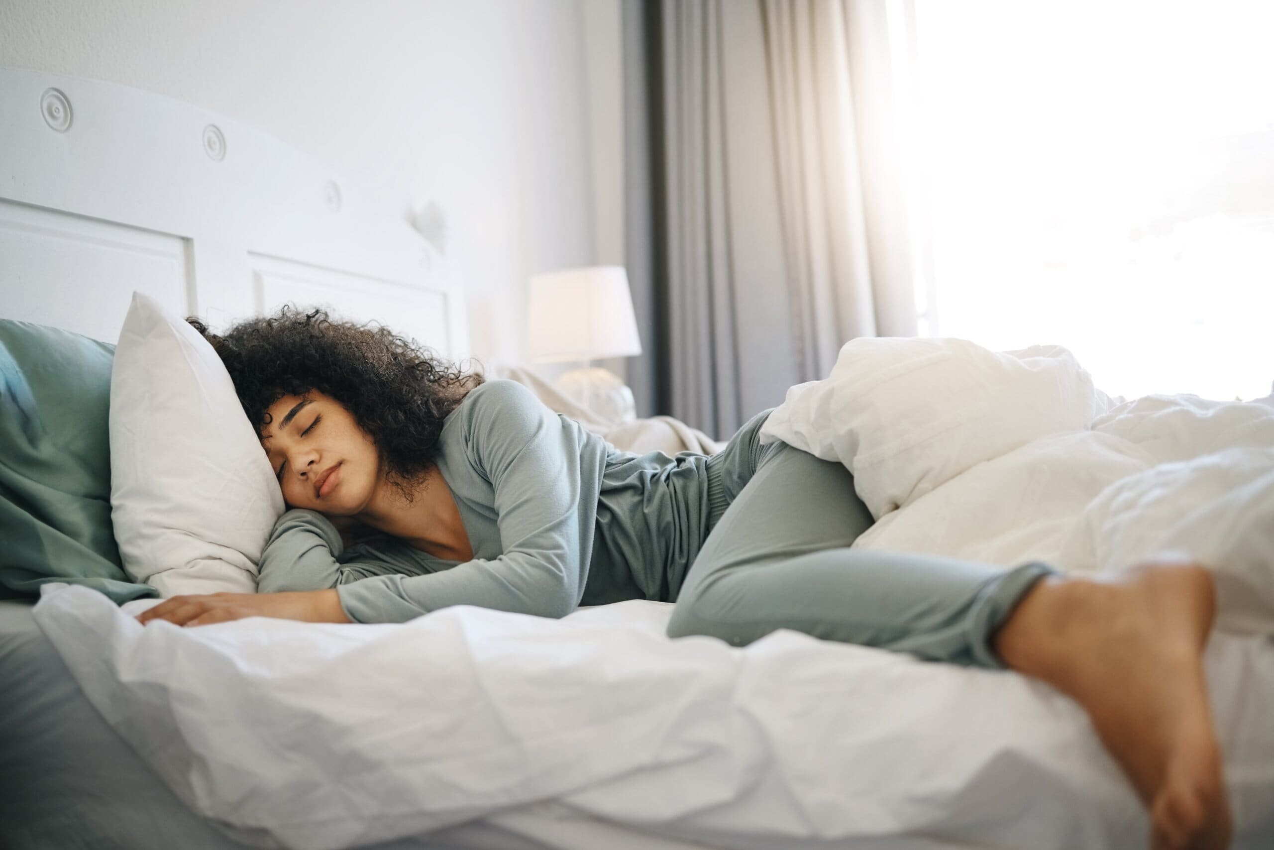 Woman sleeping peacefully on her side in bed with her foot hanging over the edge.