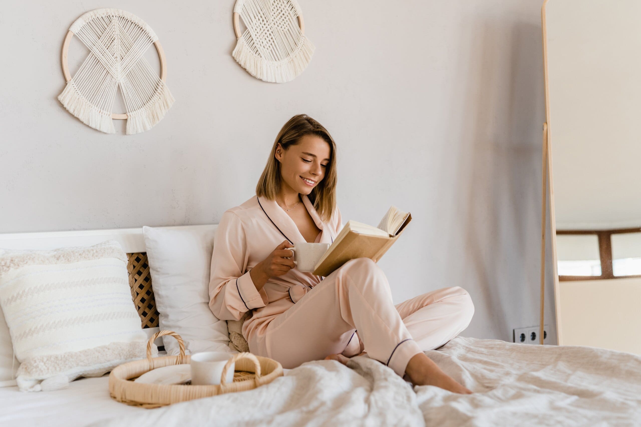 Woman smiling as she relaxes reading a book sat up in bed.