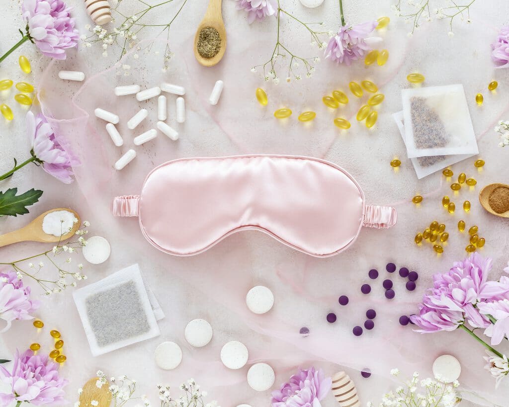 Pink sleep mask surrounded by an array of herbs, tablets and tea bags.
