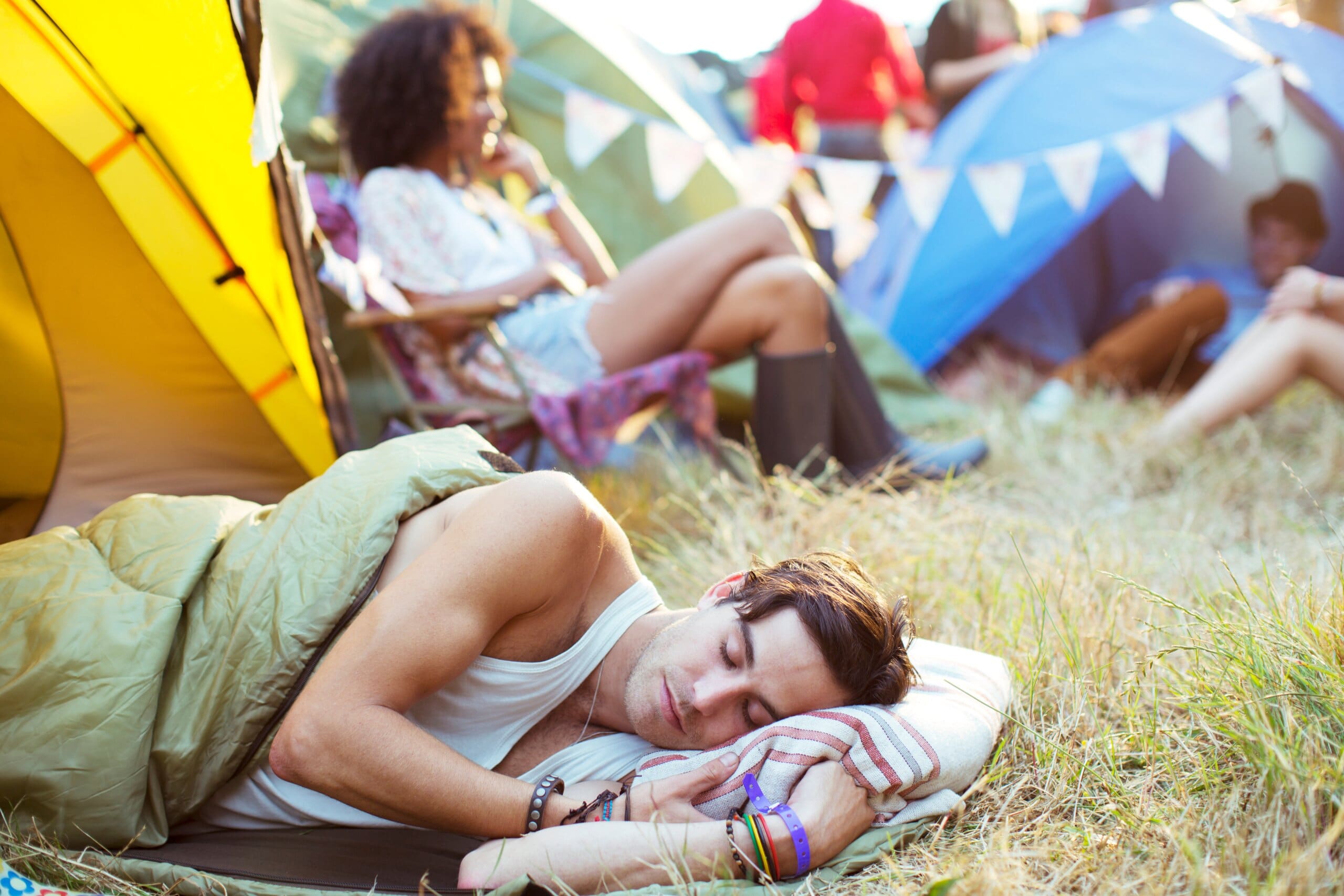 Man sleeping on grass outside of a tent at a music festival.