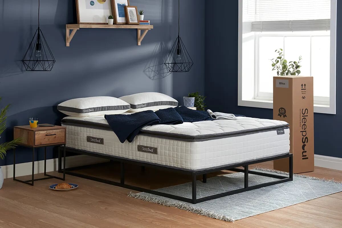 Image of the sleepsoul bliss pillow top mattress in a blue bedroom with black accessories. The mattress box stood upright to the right.