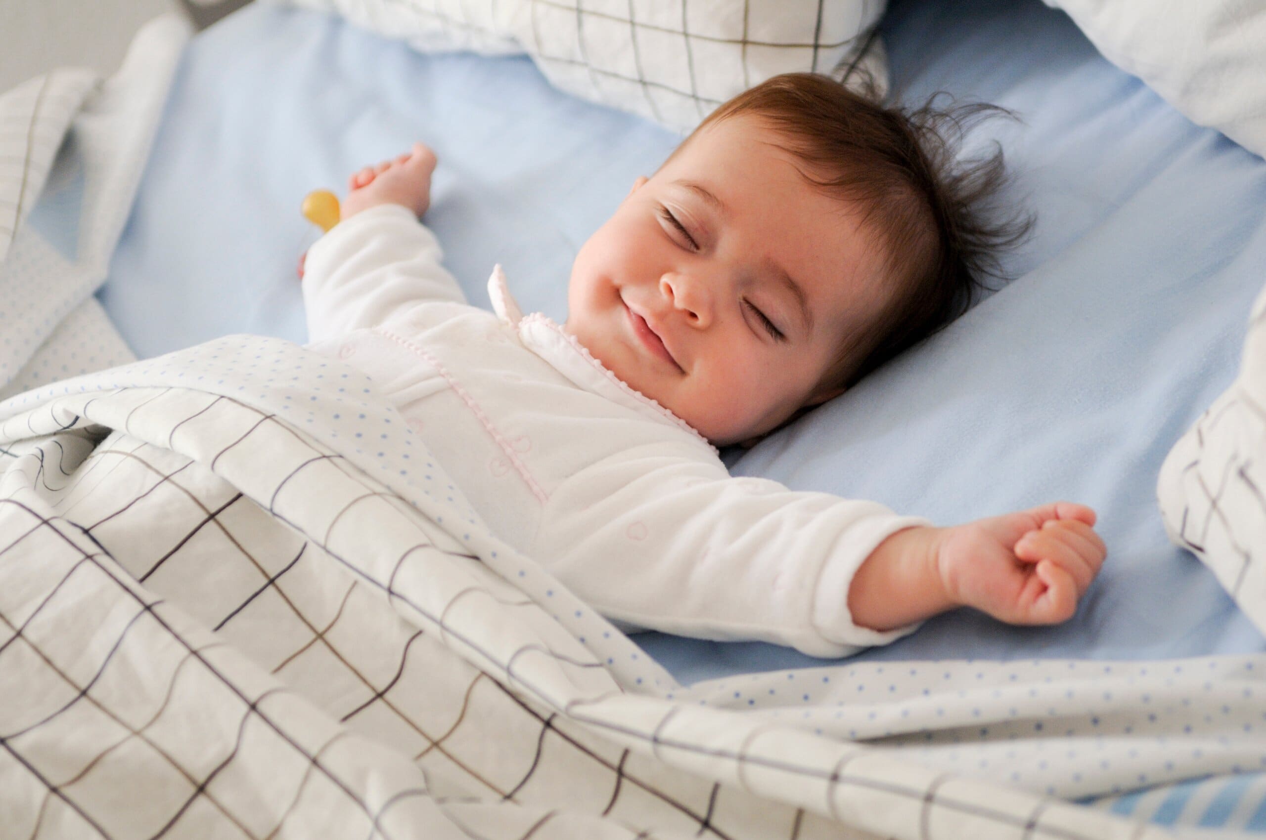 Smiling baby with arms stretched out laying in bed.