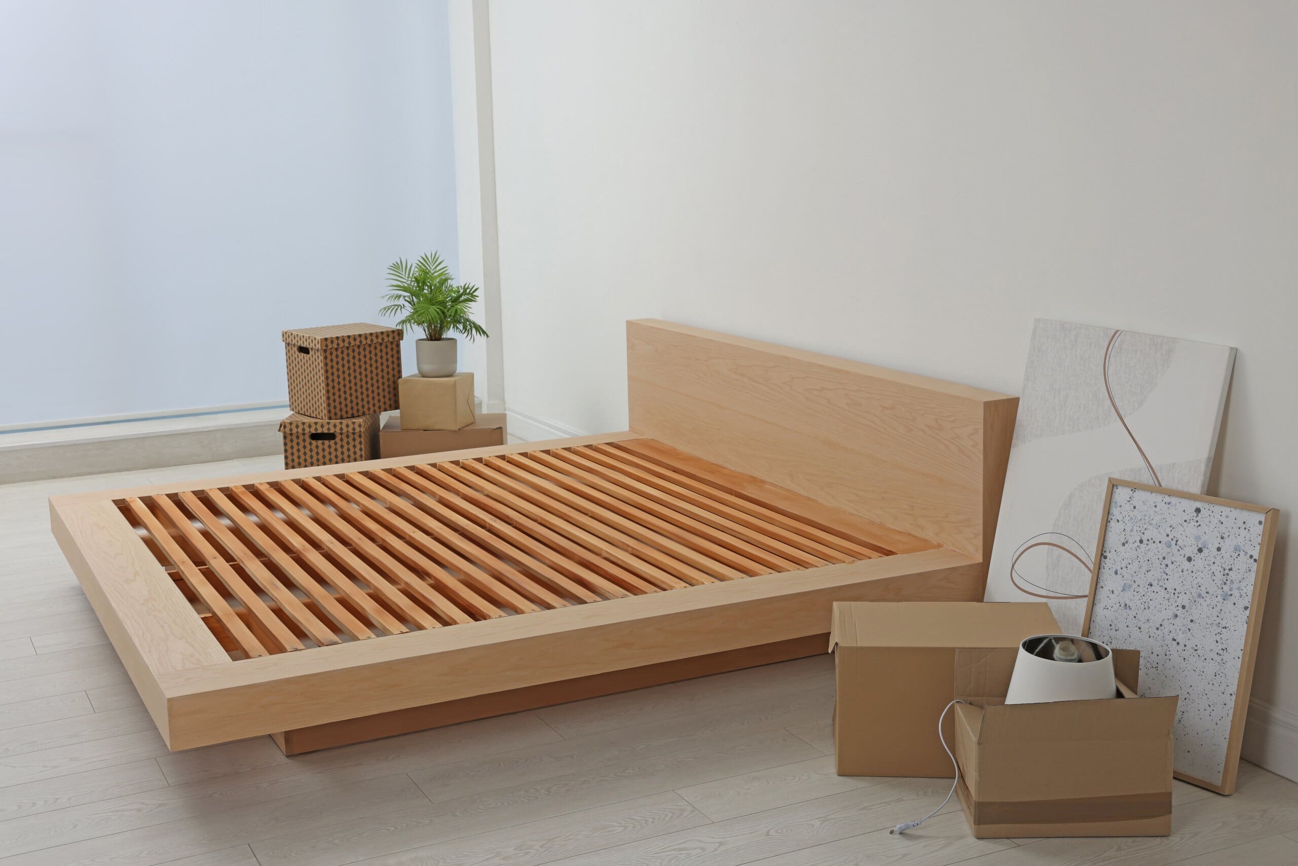 New wooden bed frame, moving boxes and decor elements indoors.