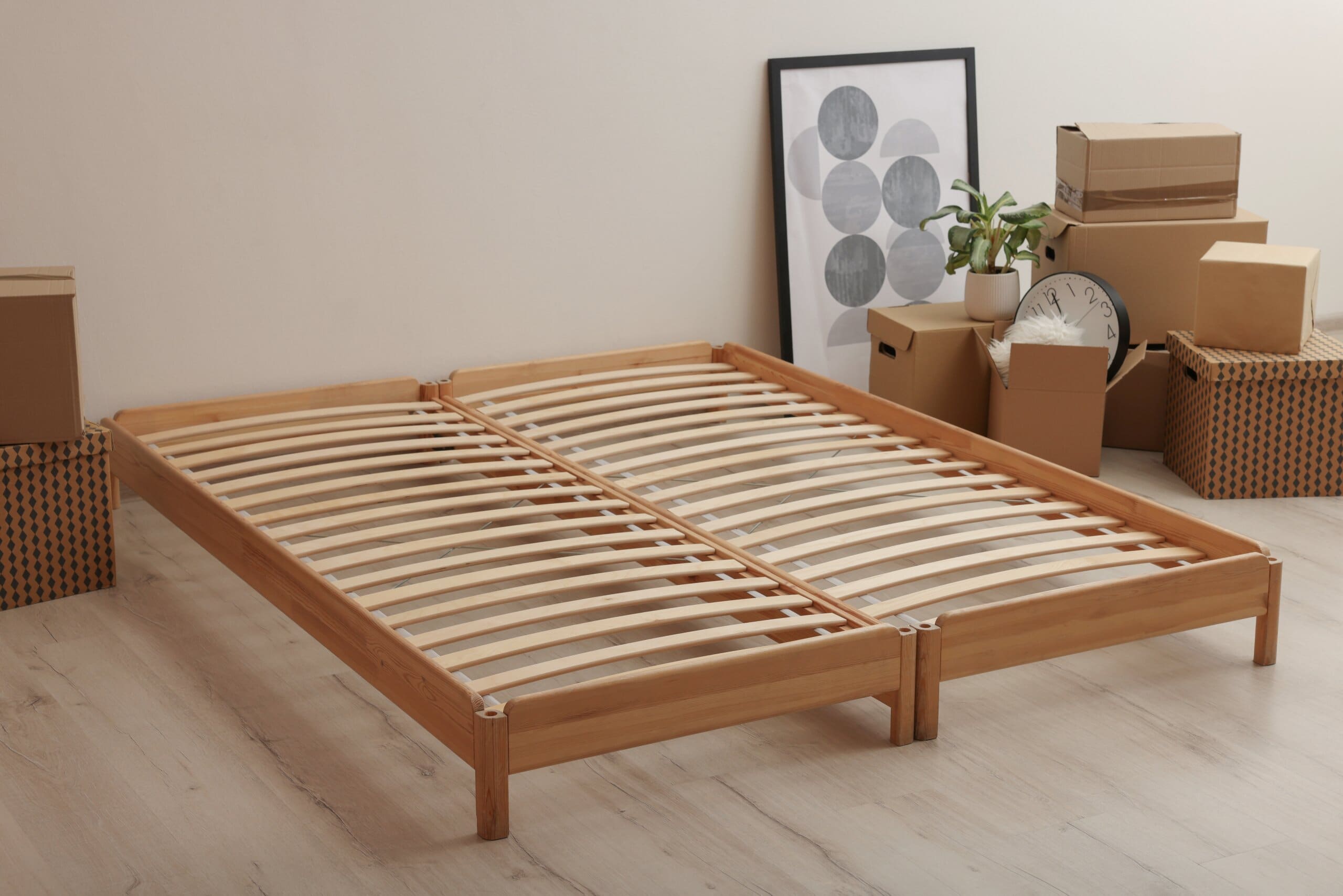 Wooden sprung slatted bed frame with moving boxes and belongings next to it.