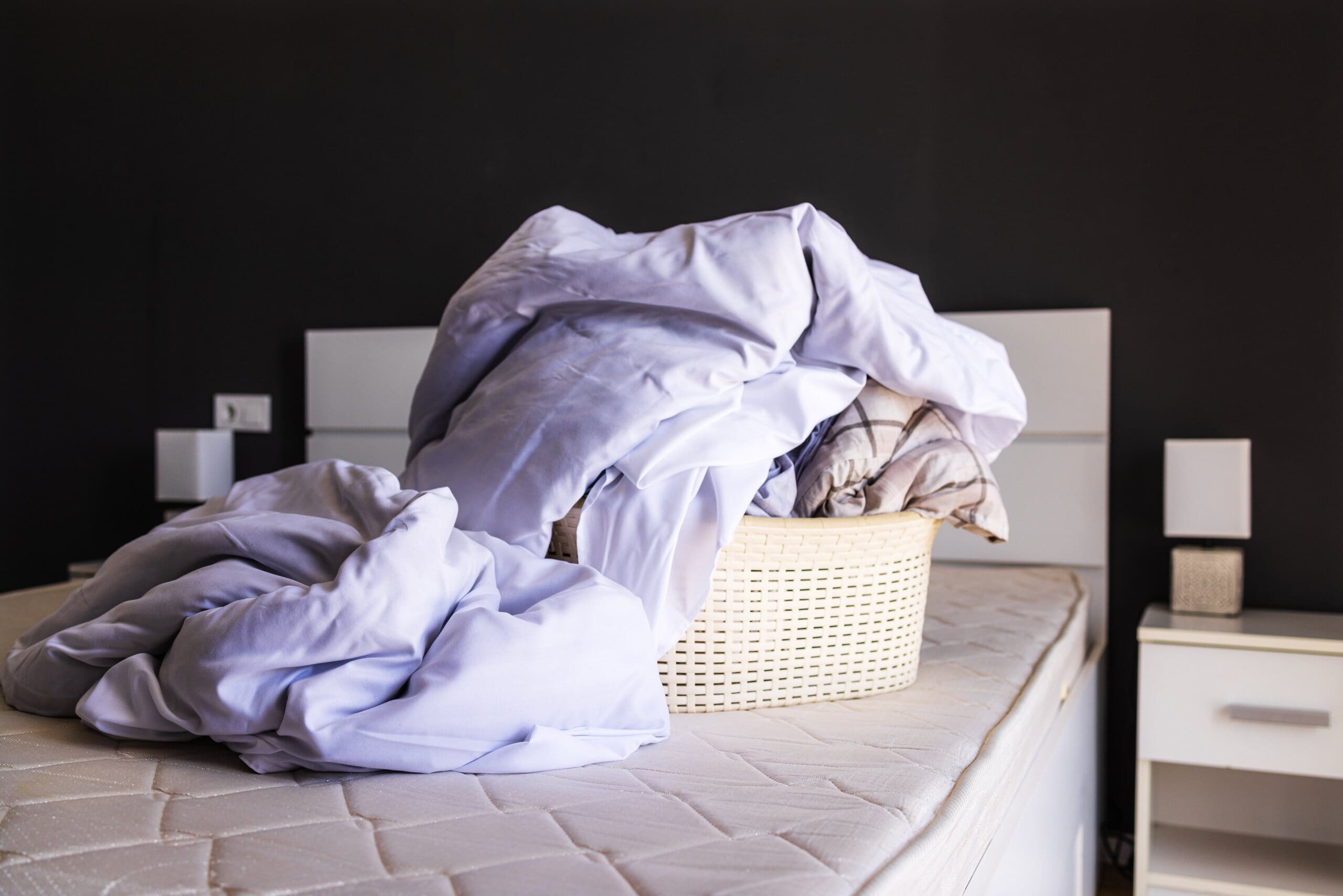 Image of an overflowing laundry basket on top of a stripped bed.