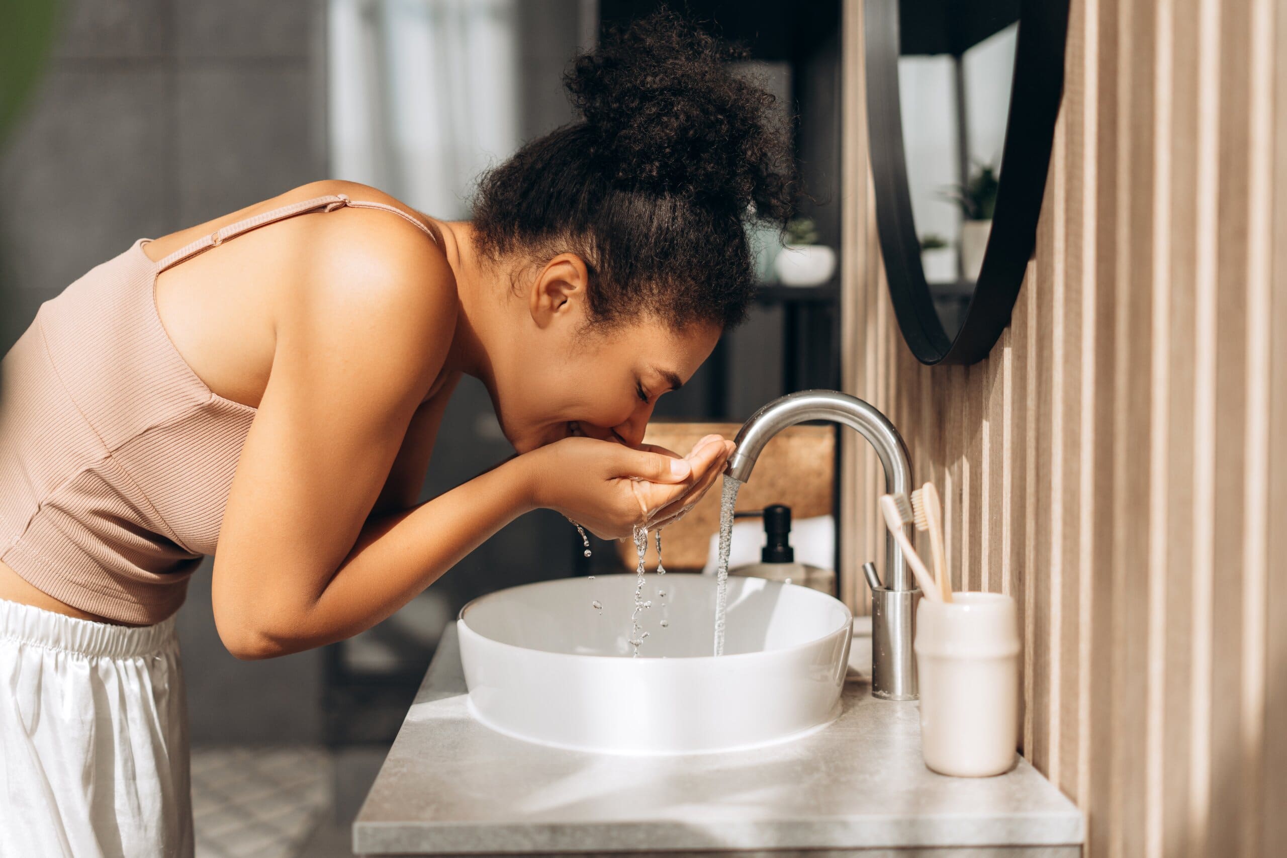 Young woman washing her face in a sink, smiling.