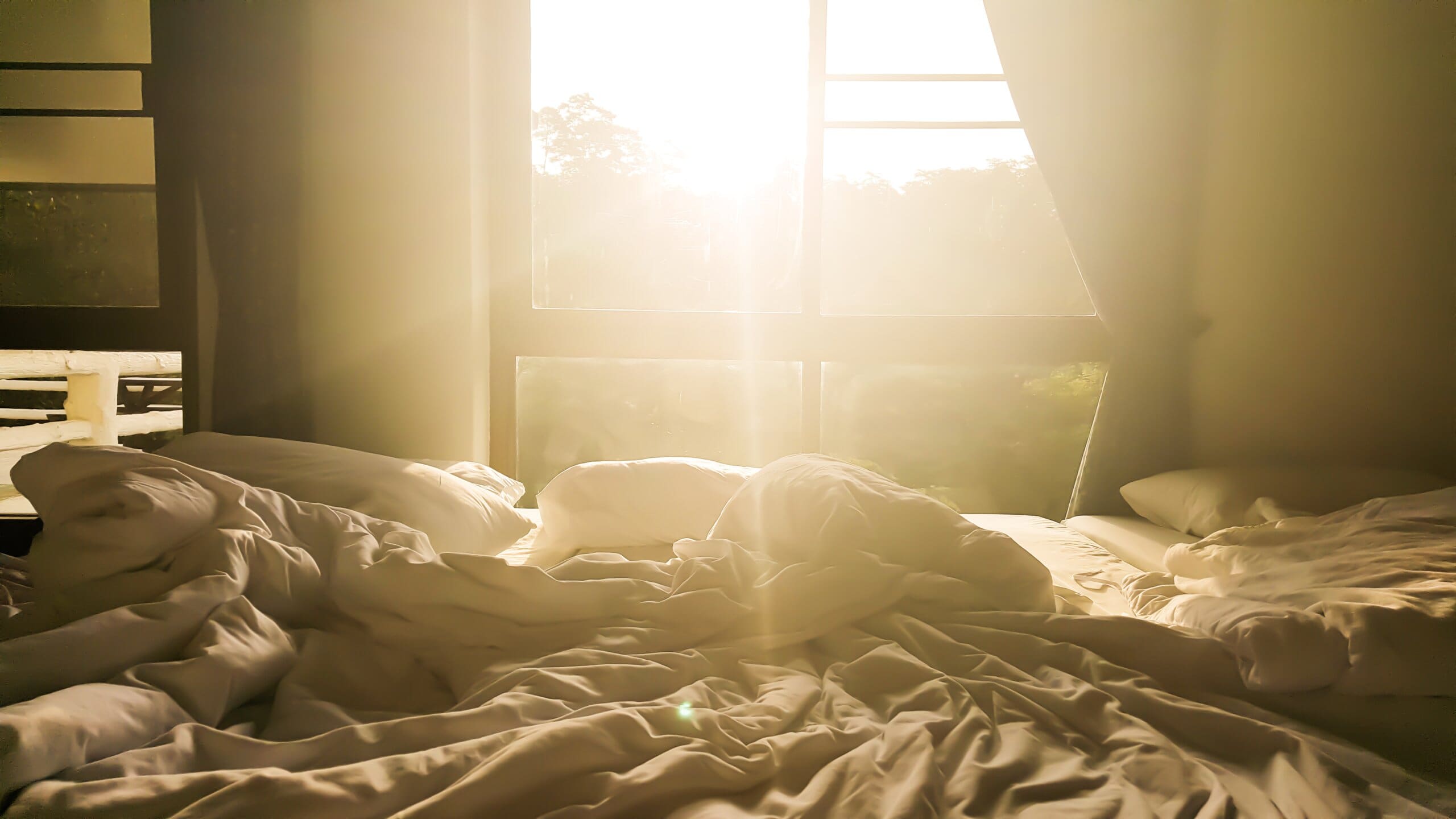 Sunlight coming through the window, shining onto an unmade bed.