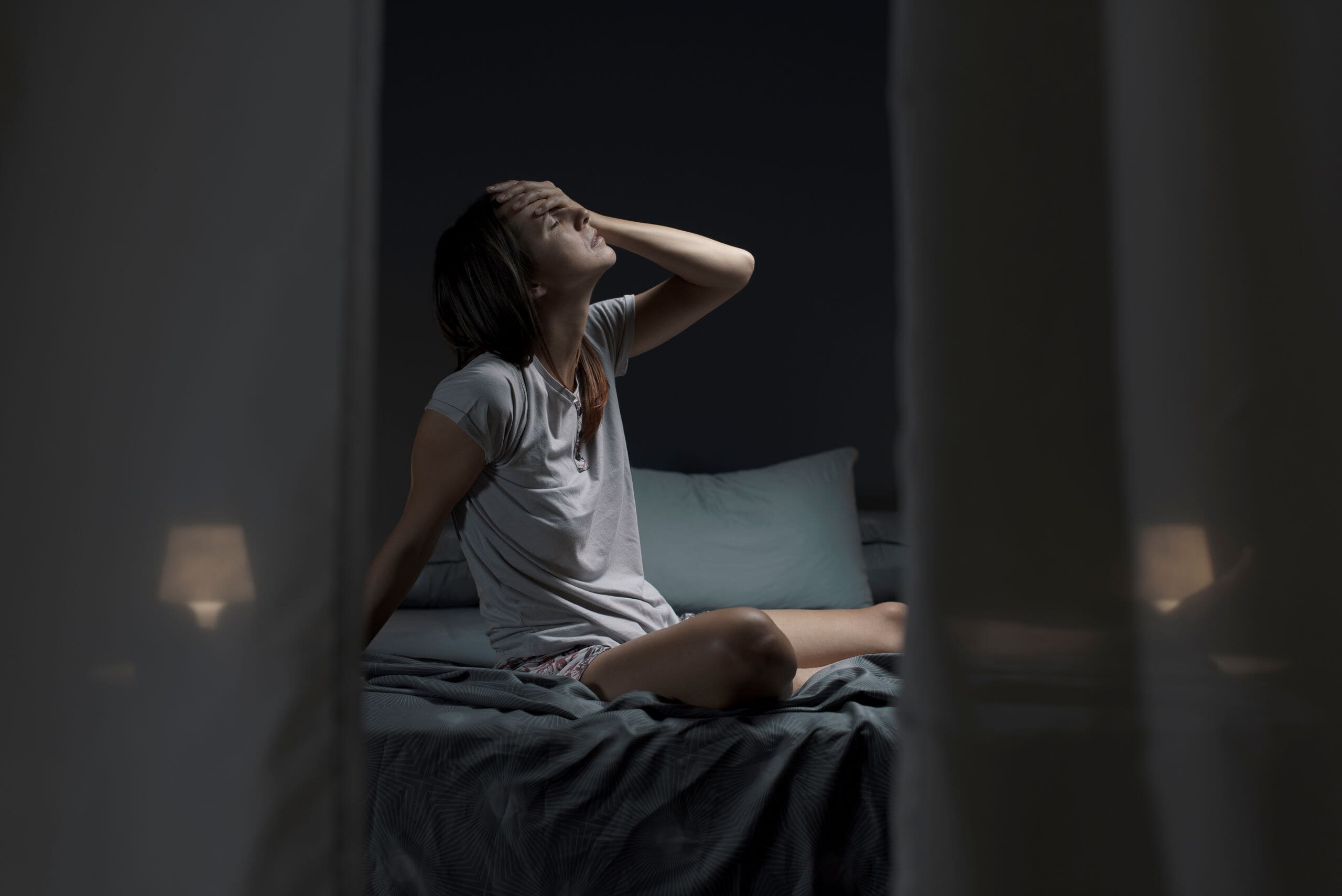 Woman sat up in bed unable to sleep with night sweats.