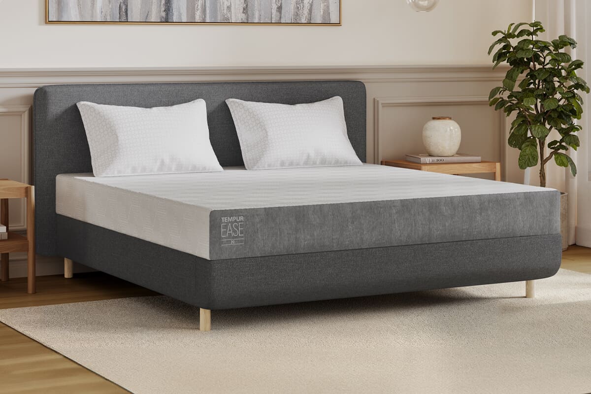 A Tempur mattress on a grey upholstered bed frame in a neutral coloured bedroom.