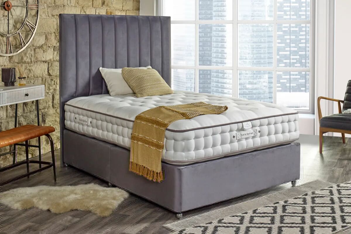 Image of a luxury orthopaedic mattress on a grey divan bed in a neutral coloured bedroom.