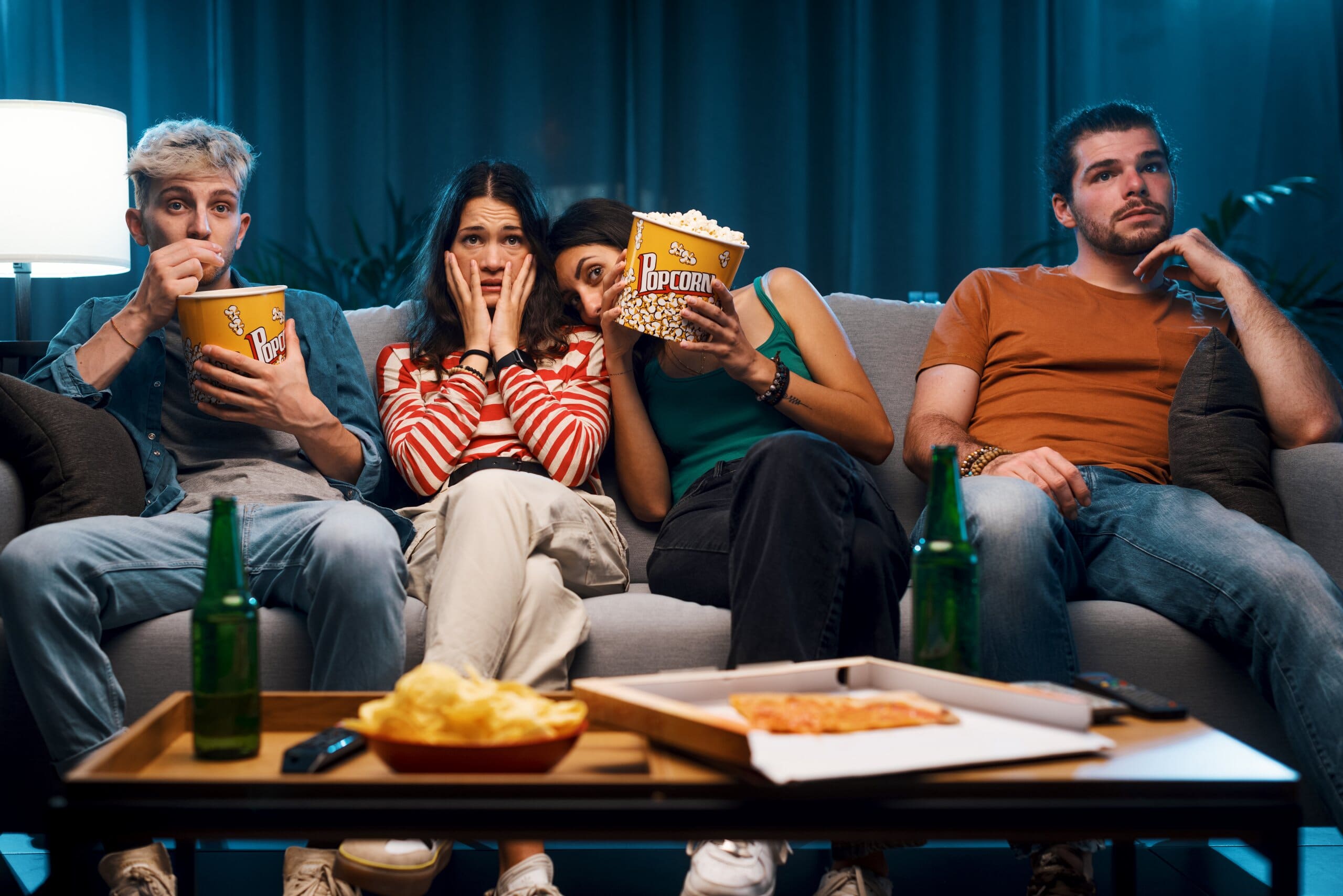 Group of four friends sitting on sofa with popcorn watching a scary film.