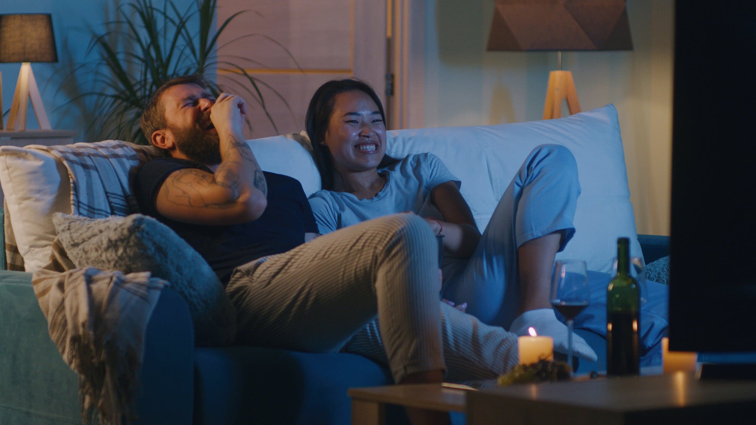 Couple sat on sofa laughing watching TV.