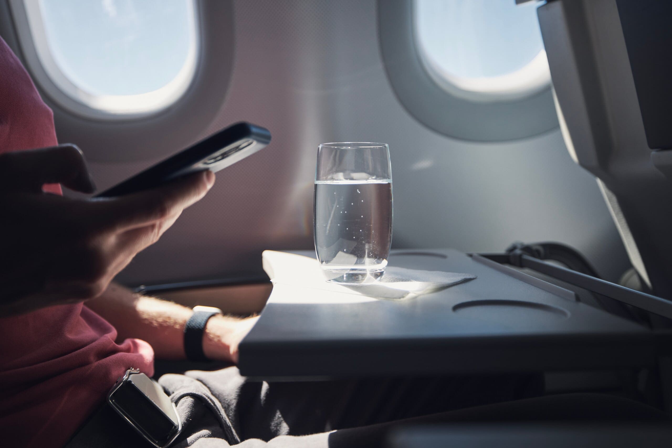 Glass of water on the tray table of a passenger's seat on a plane.