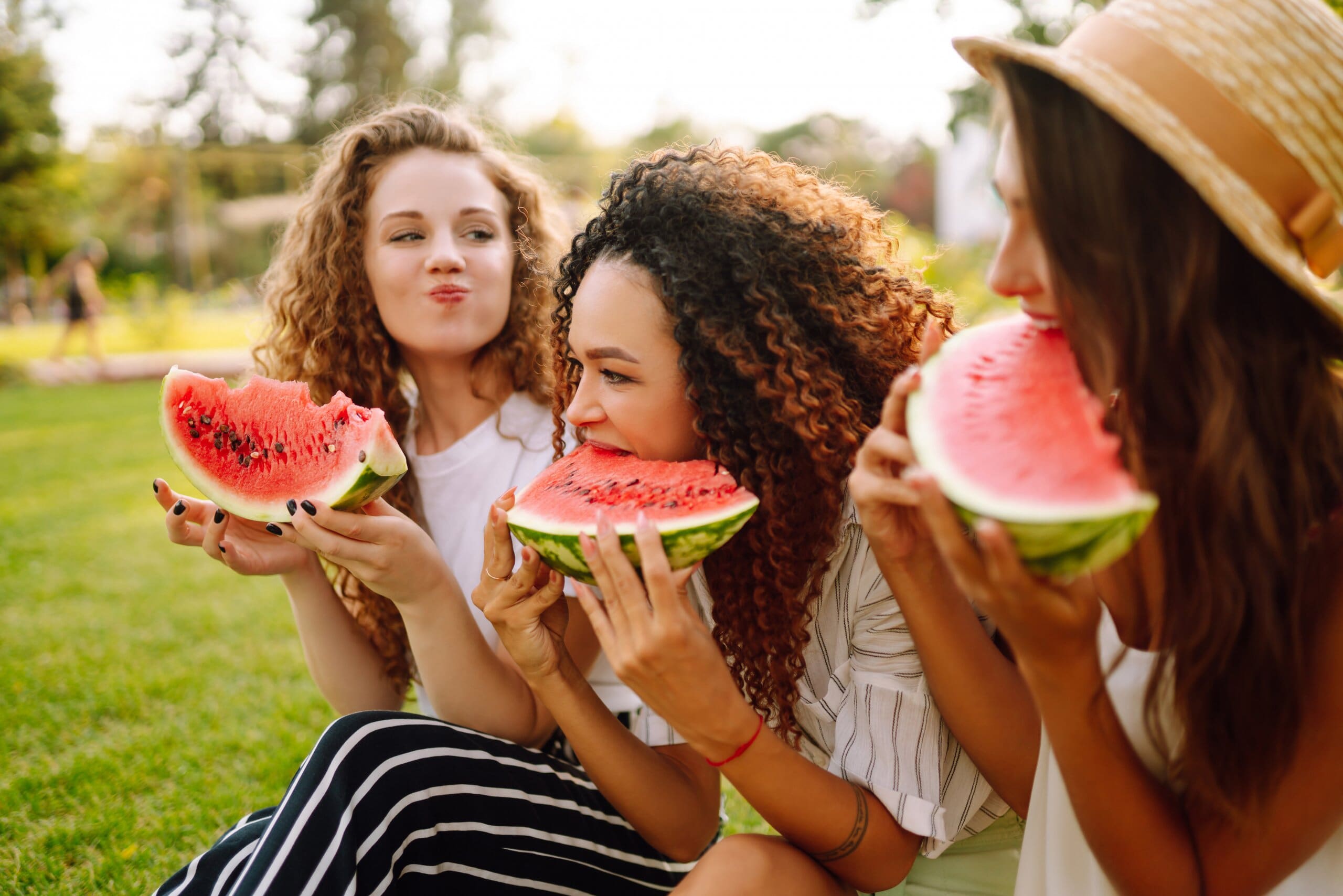 3 girls sat together eating large pieces of watermelon.