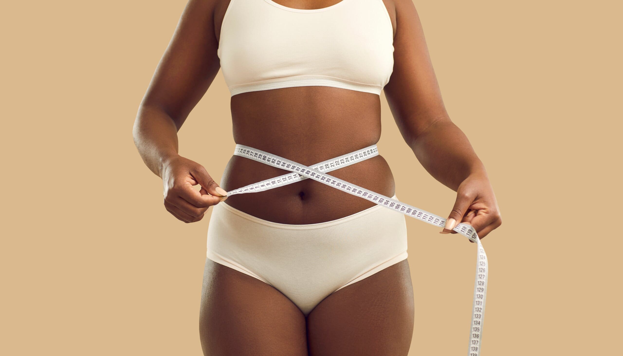 Woman in underwear holding tape measure around her waist.