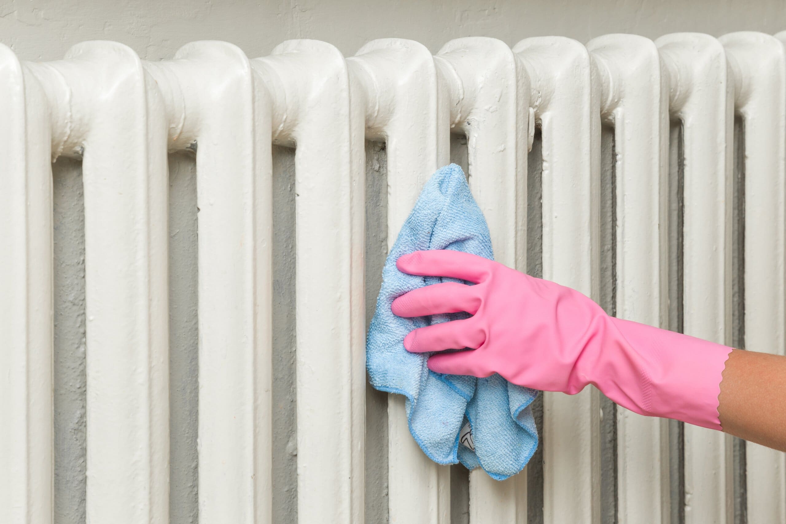 Hands with pink gloves on wiping a cloth over a radiator.