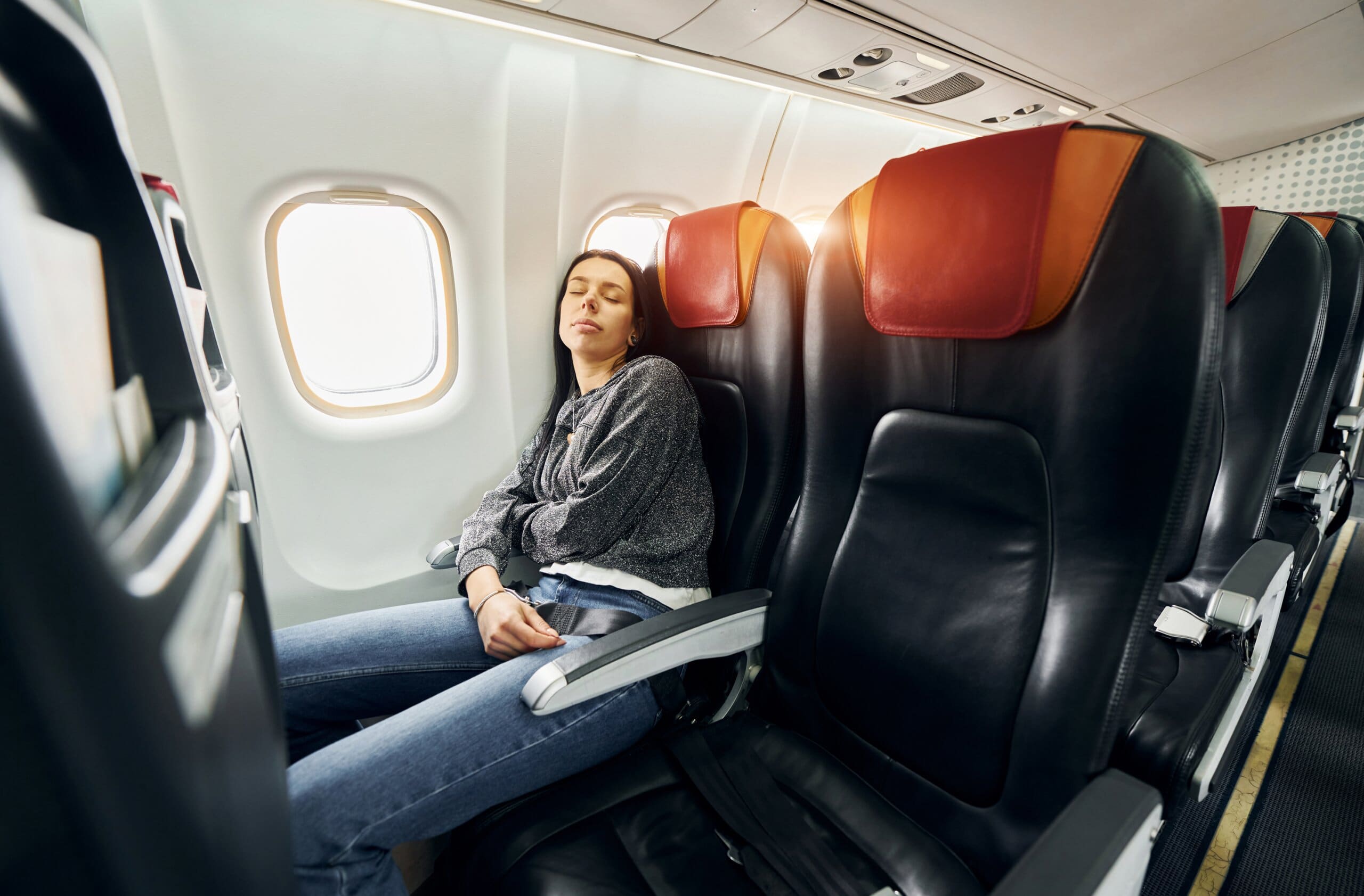 Woman sleeping in window seat on a plane with empty seats beside her.