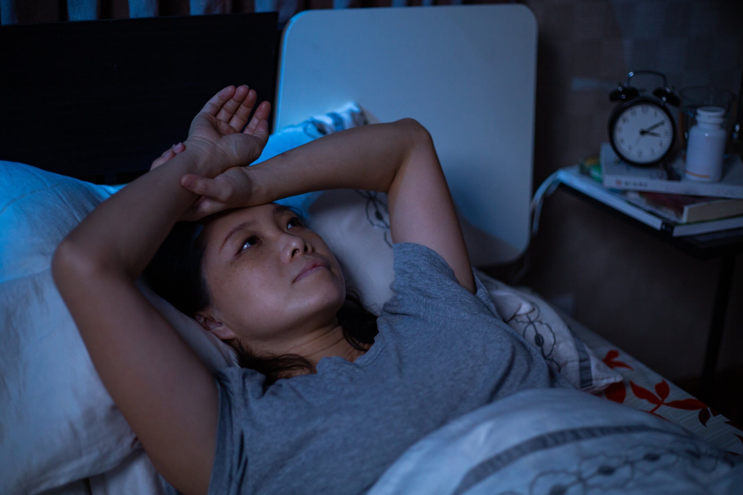 Woman looking annoyed staring at the ceiling in bed as she can't sleep.